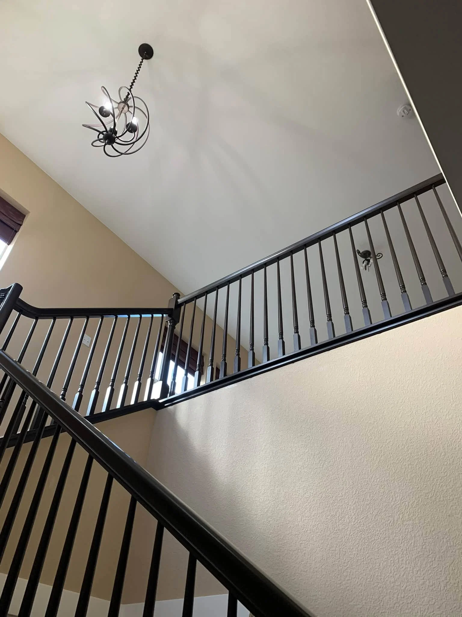 Interior view of a staircase with black metal railing, beige walls, and a modern black chandelier hanging from the ceiling.
