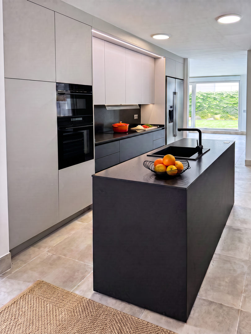 Cocina moderna con isla negra, electrodomésticos integrados, gabinetes blancos y una vista de jardín con césped a través de una ventana grande.