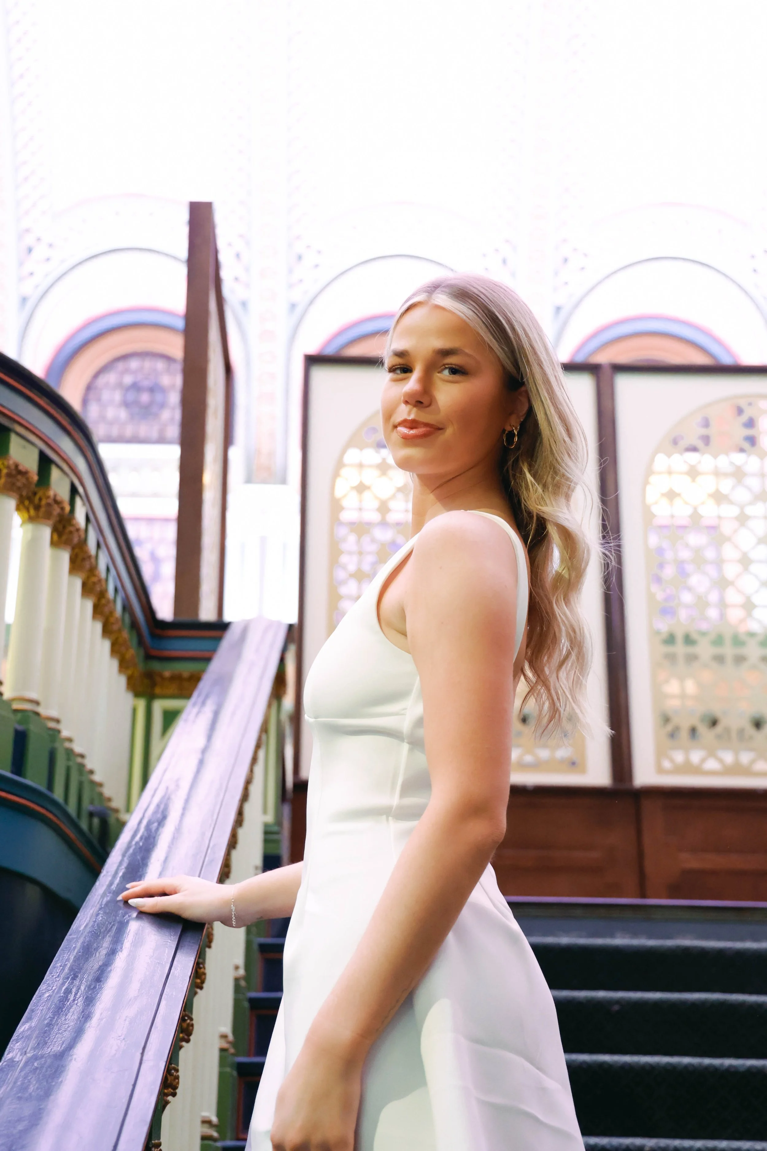 A young woman in a white dress standing by a church organ, inside a church with stained glass windows and an ornate wooden interior.