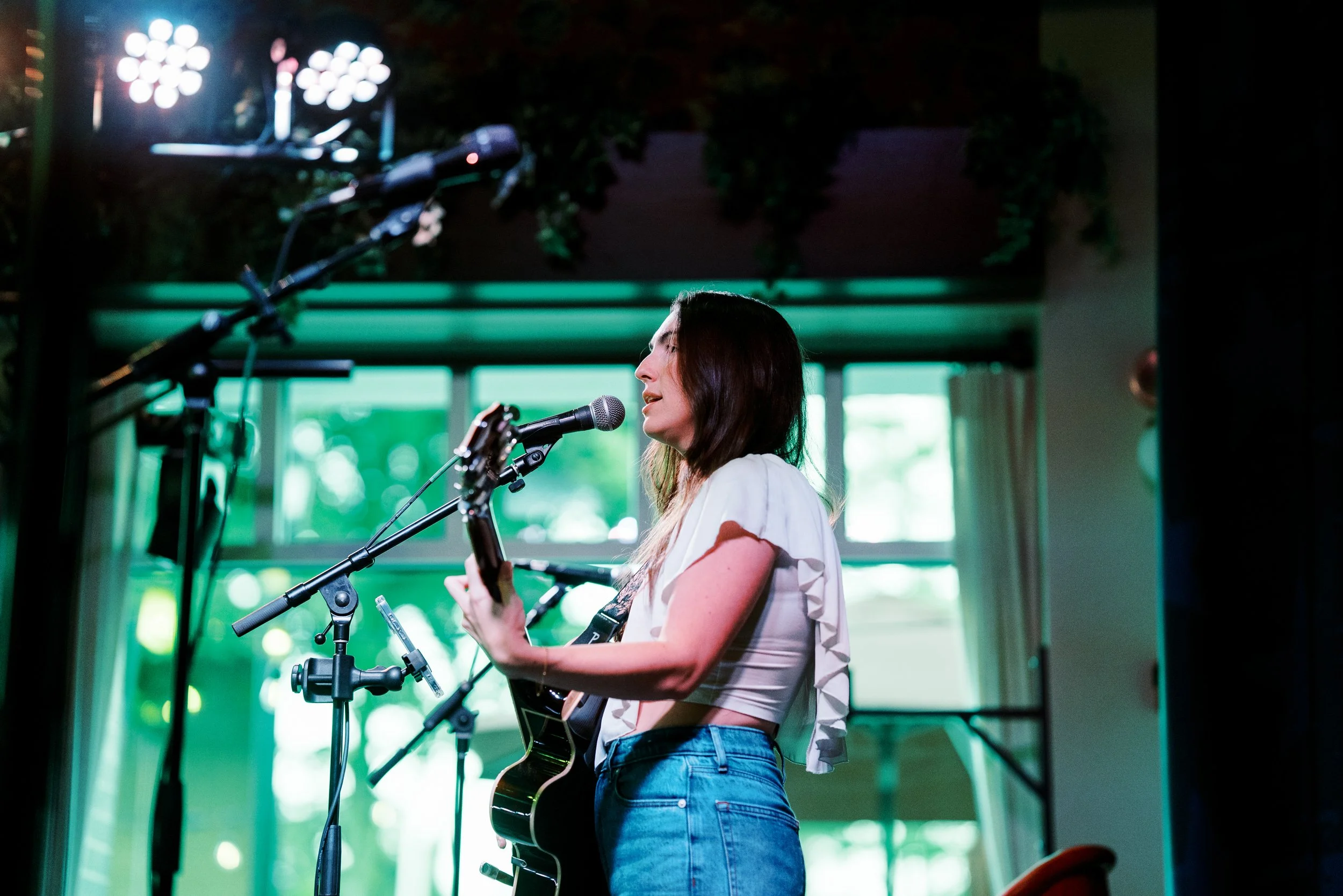 Young woman playing an acoustic guitar and singing into a microphone during a performance.
