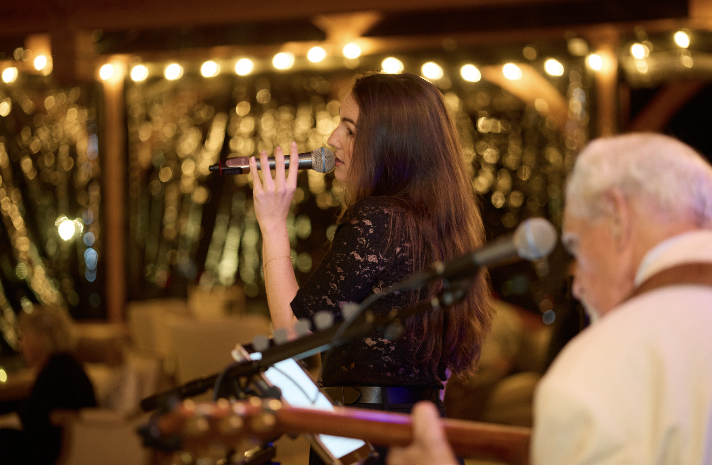 A woman singing into a microphone while playing the keyboard during a performance in a warmly lit indoor venue.