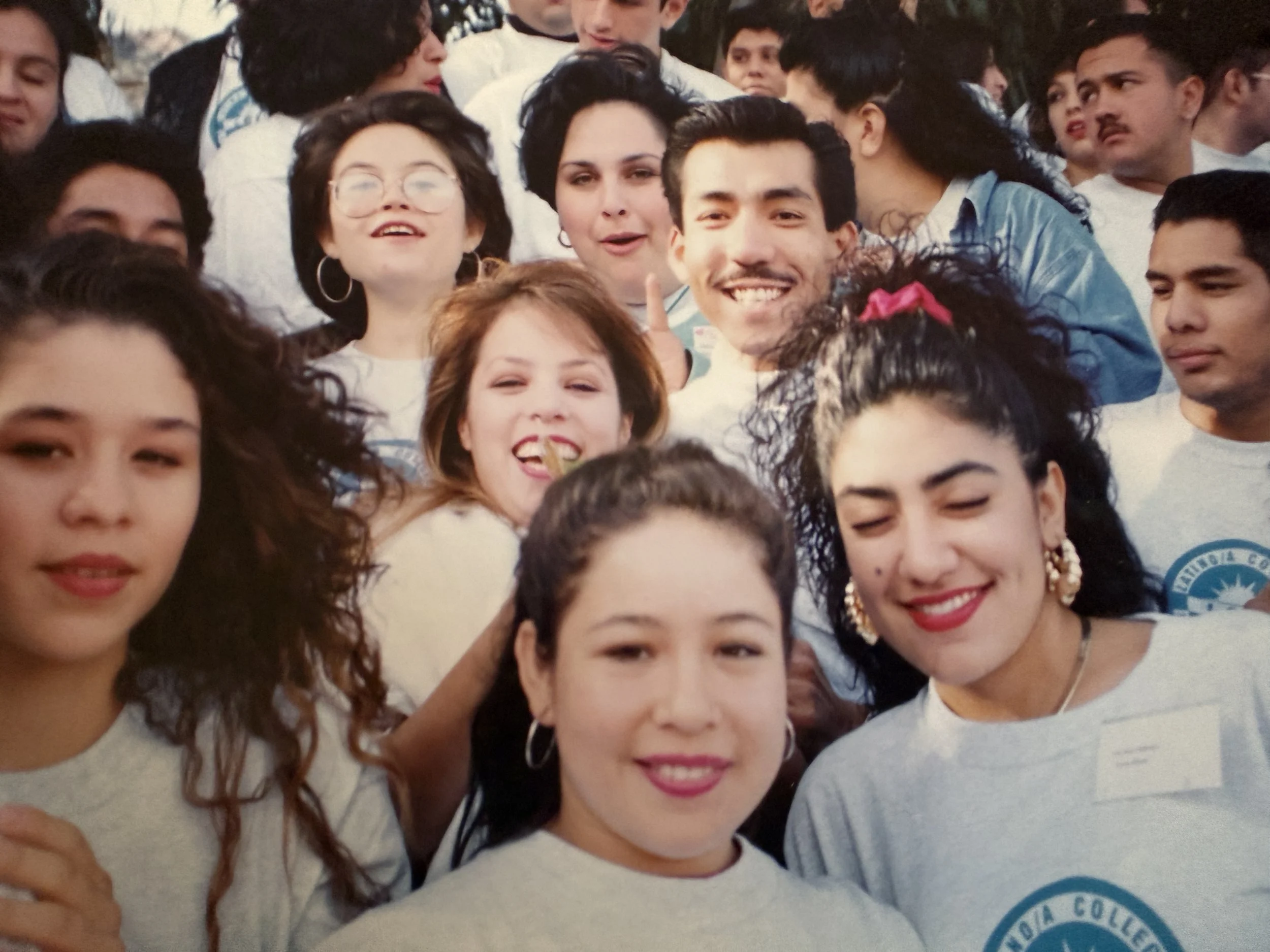 Group of diverse young people smiling and posing for a photo, wearing casual clothing, outdoors during daytime.