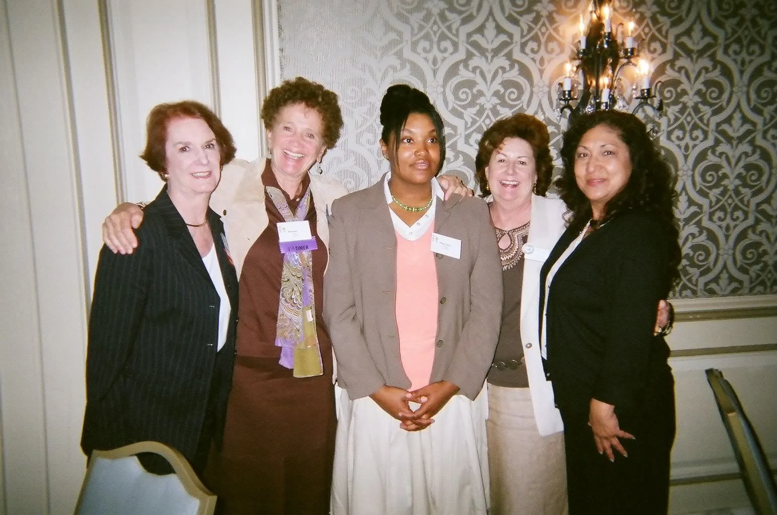 Six women standing together in a formal setting, smiling and posing for a photo.