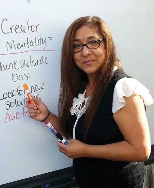 Woman standing in front of a whiteboard, writing with markers, with text about creator mentality, outside the box thinking, and seeking new solutions.