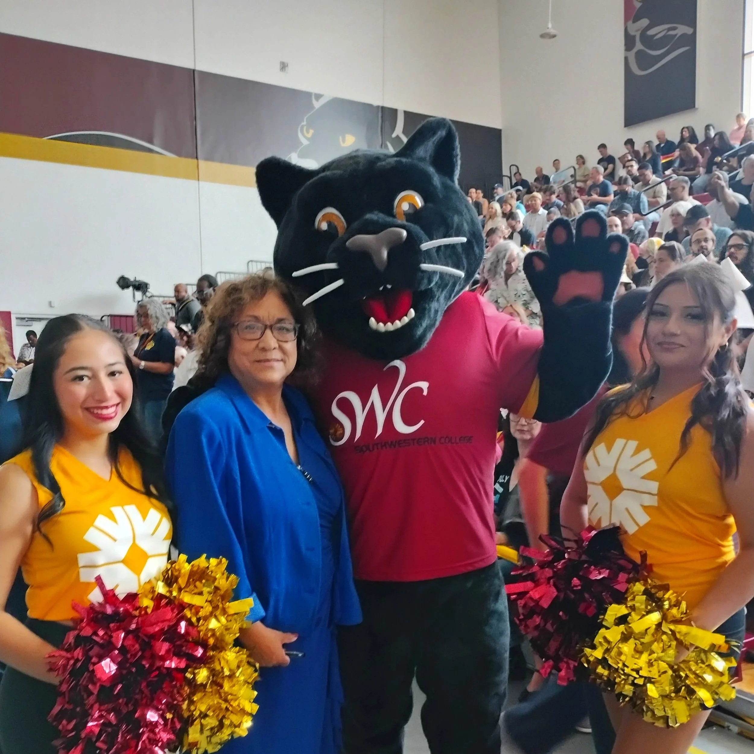 People at a crowded indoor event, some wearing mascot costumes, with one person in a large black panther costume waving.