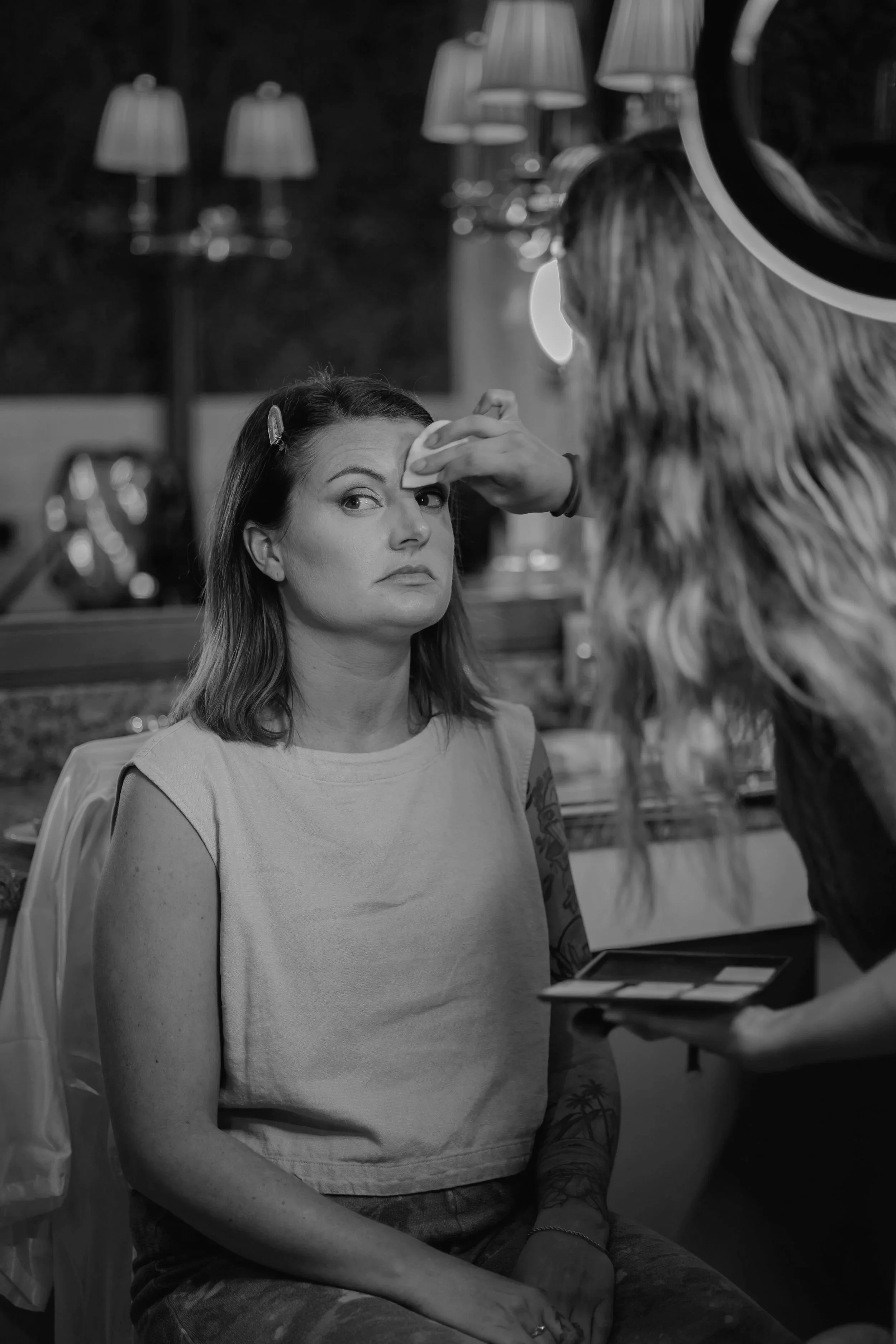 A woman sitting on a chair, having her makeup done by Bria, a professional makeup artist in Madison, WI.