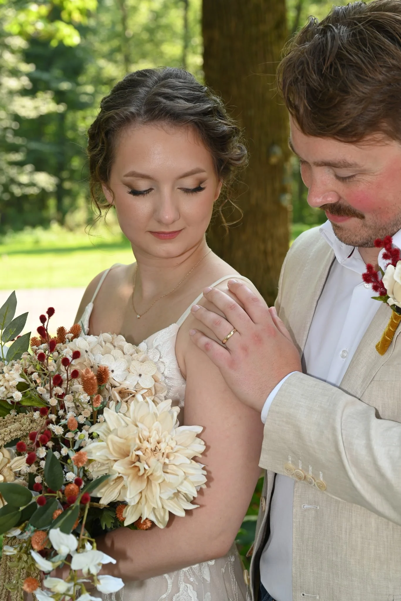 A bride and groom during their wedding ceremony outdoors, exchanging vows or rings with a bouquet of flowers in the foreground and a background of trees, greenery, and makeup in Madison, WI.