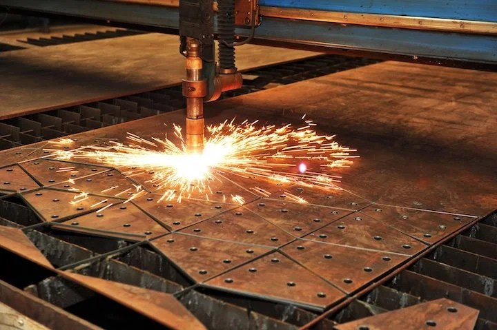 A laser cutting machine cutting a metal sheet with sparks flying.