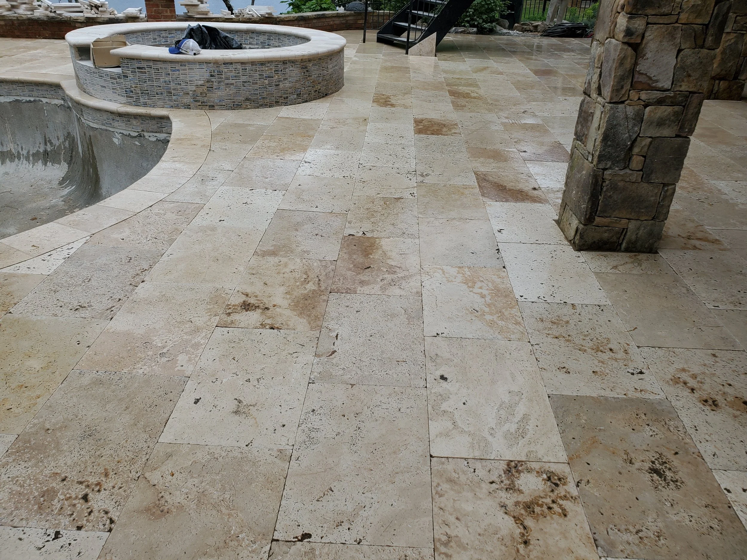 Backyard patio with stone flooring, a hot tub with mosaic tile exterior, steps leading up to a garden area, and a stone pillar on the right side.