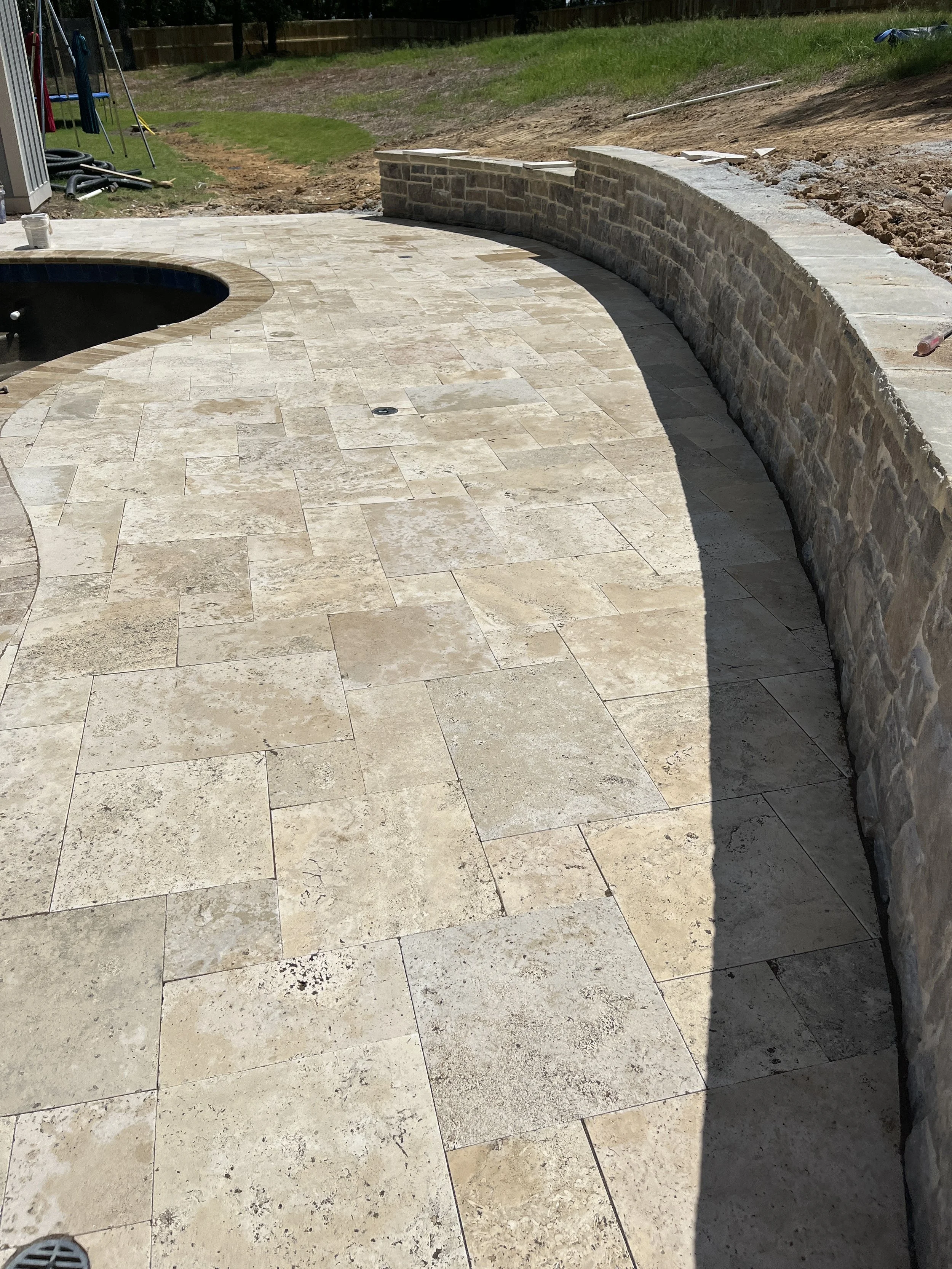 Backyard patio with stone tiles, a curved stone wall, and a grassy area under construction.