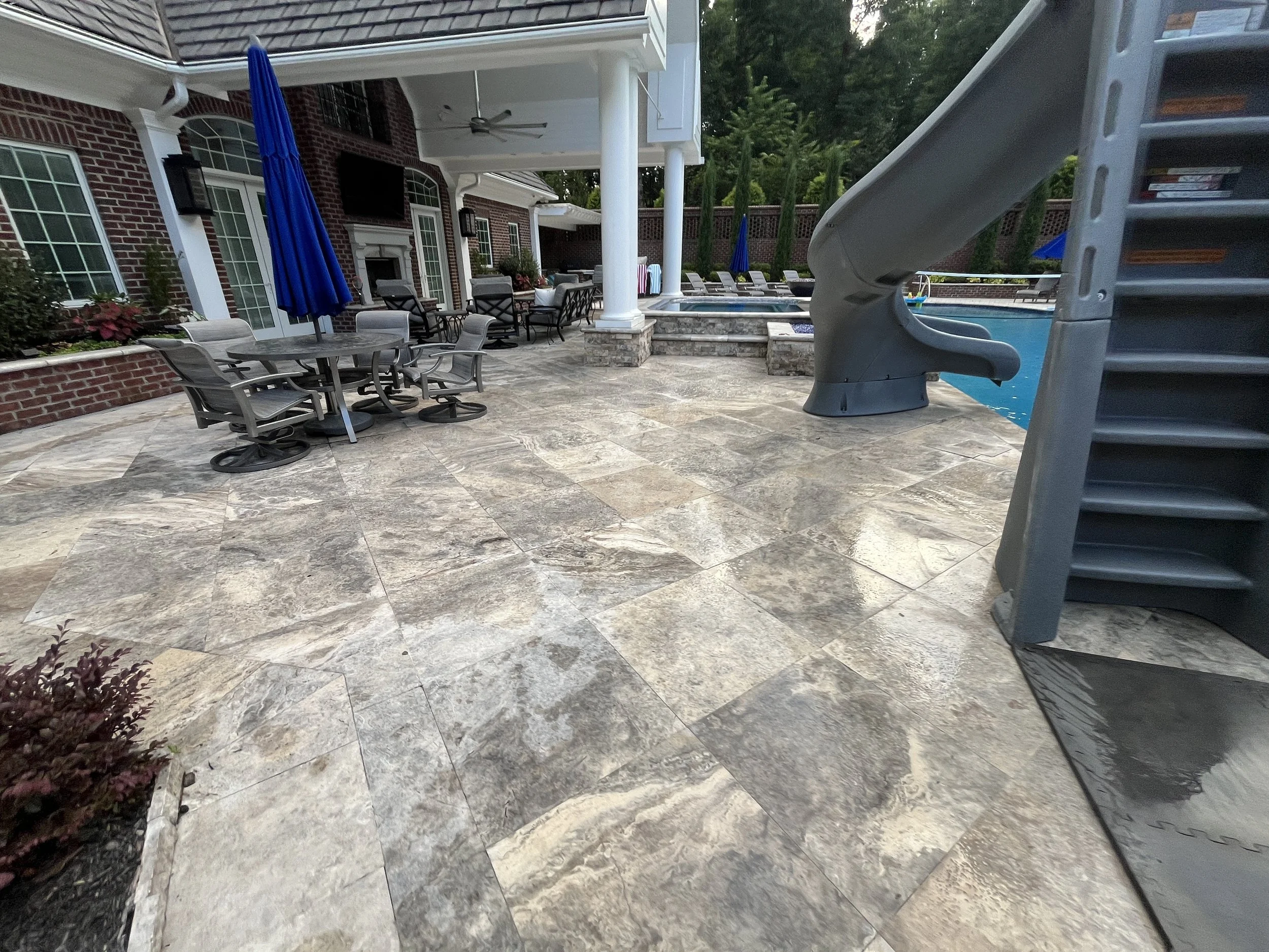 Backyard patio with a brick house, outdoor furniture, umbrellas, and a pool with a slide.
