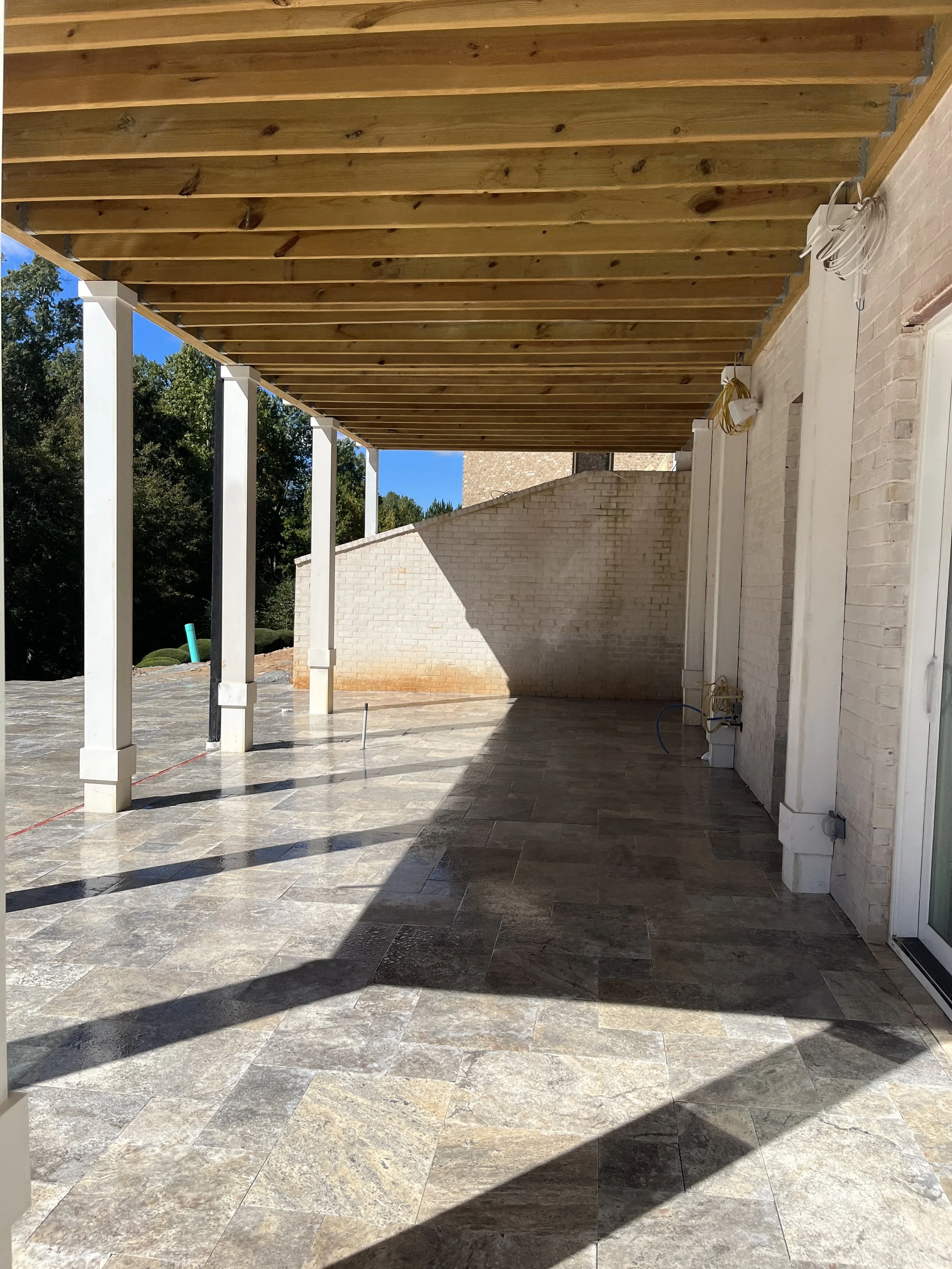 Under construction or renovation porch area with wooden ceiling, white brick wall, and tiled floor, with some electrical wiring visible.