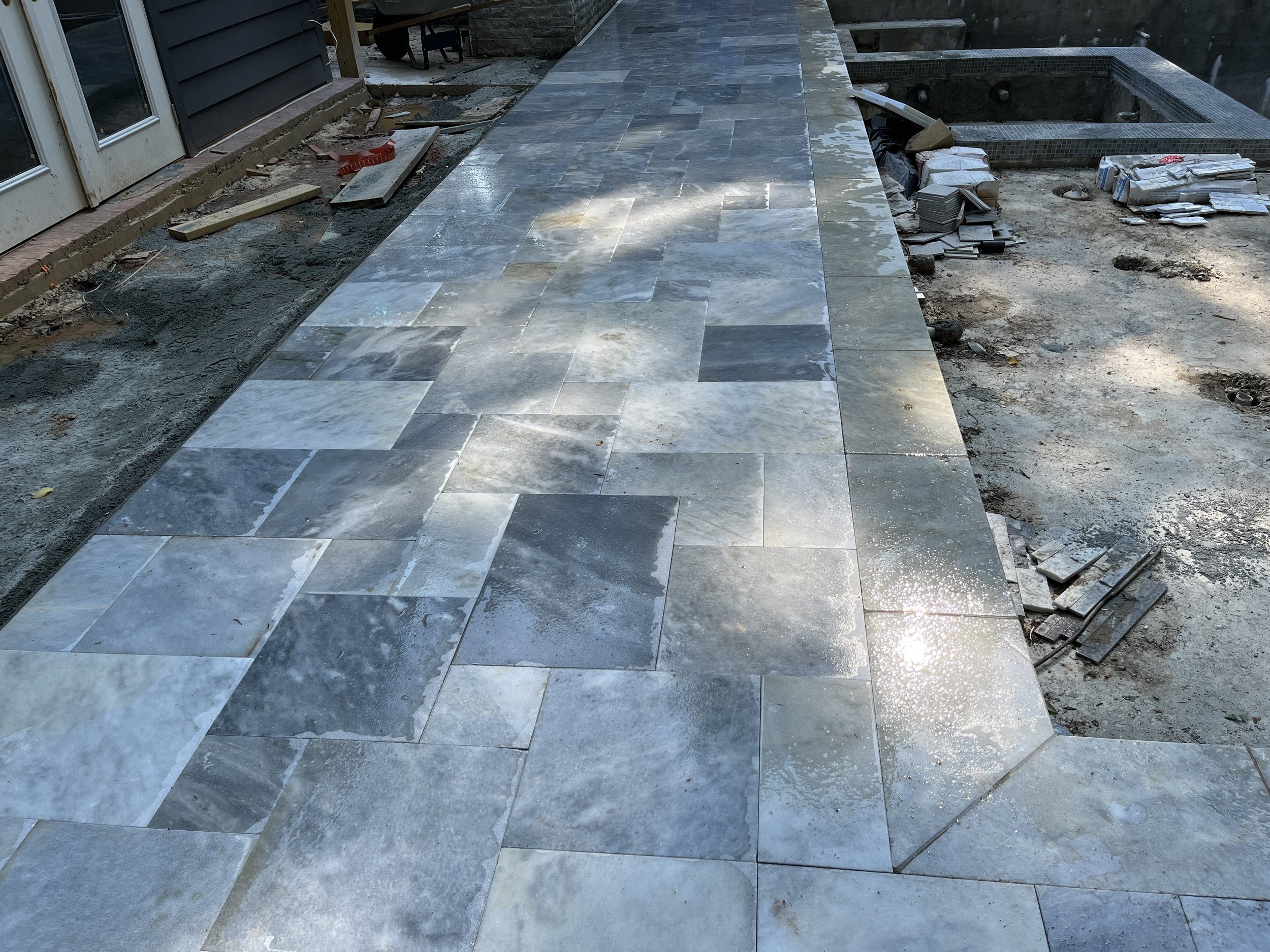 Construction site with partially completed tiled pathway and ongoing work, including scattered tiles and construction materials.