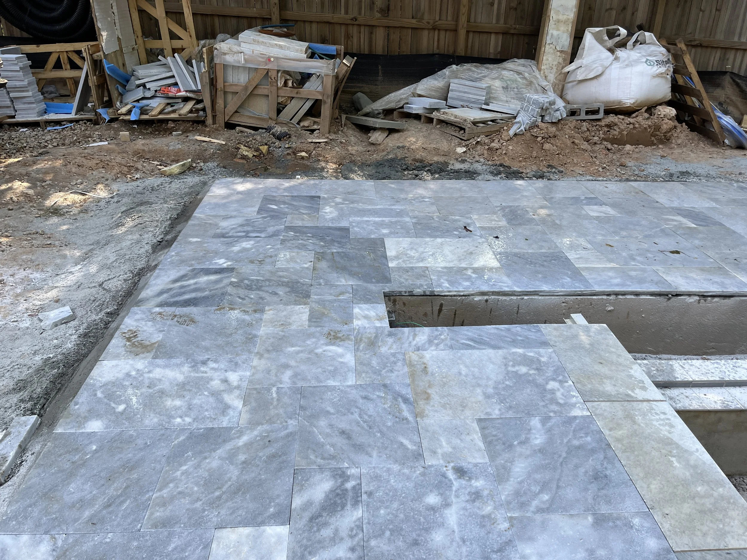 Construction site with partially completed stone or tile flooring, construction materials, and tools scattered around.