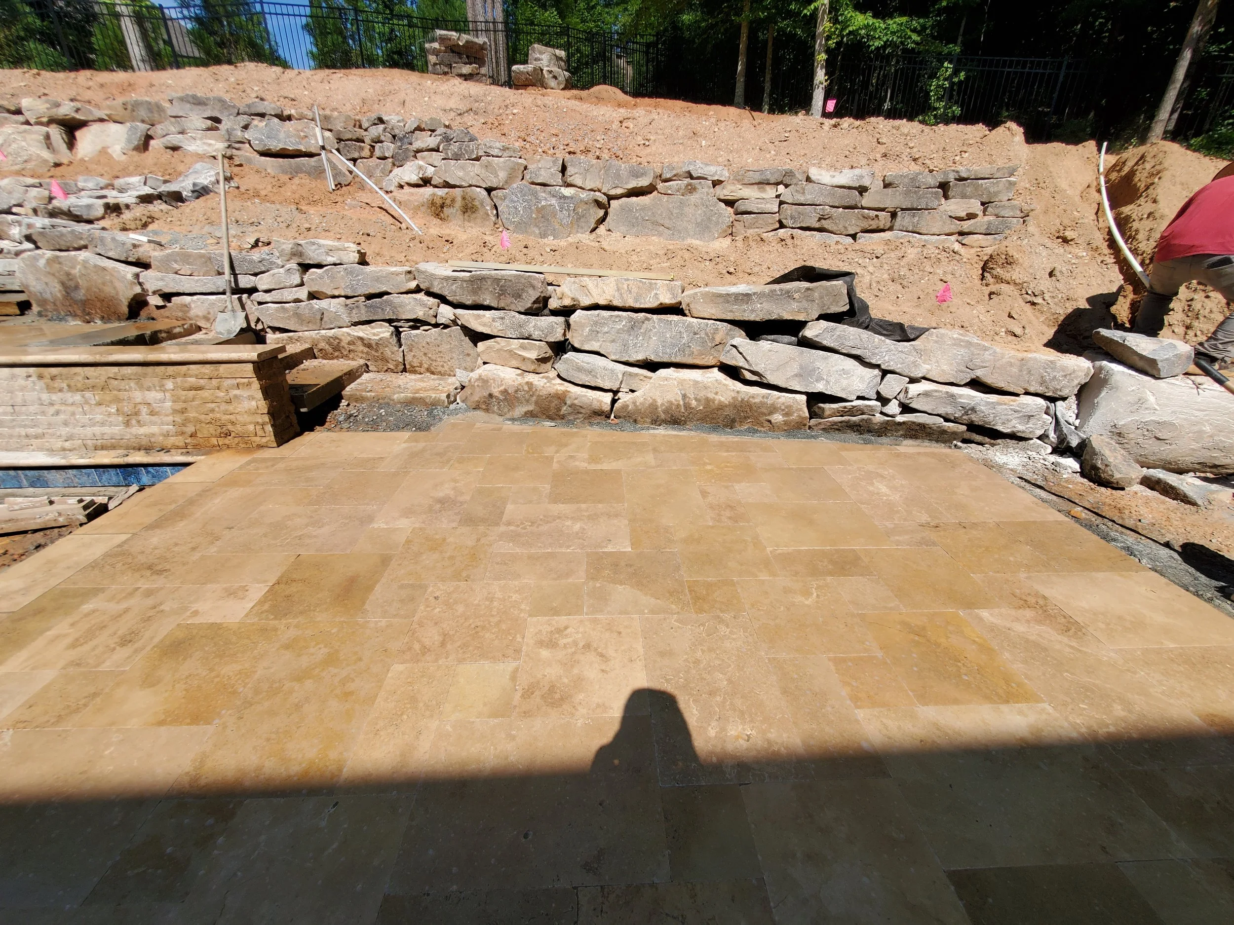 Construction site with a partially built stone wall and a worker laying stones on the right side.