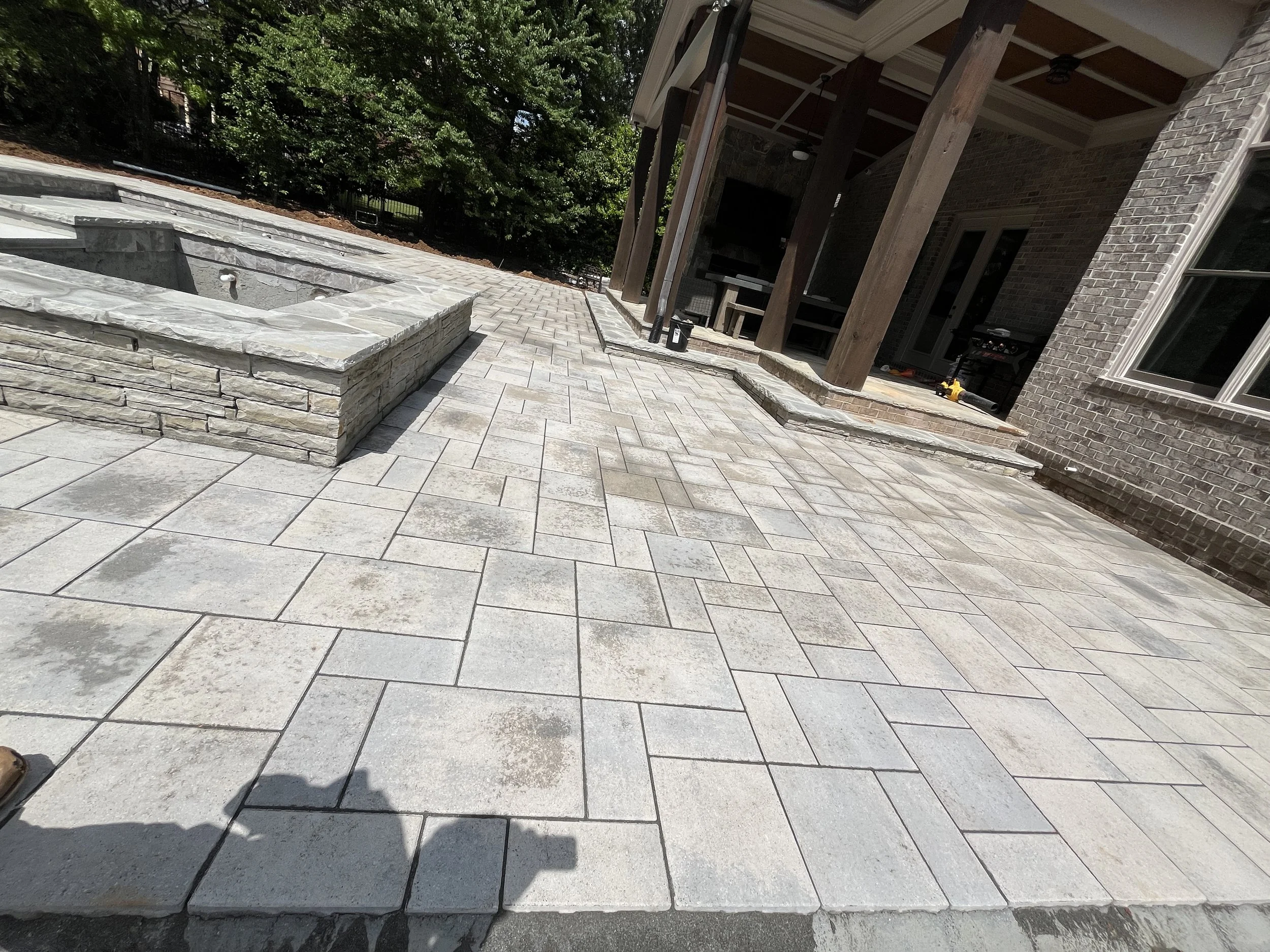 Backyard patio with stone and concrete tiles, stone fire pit, and a covered porch area with wooden support beams and brick house exterior.