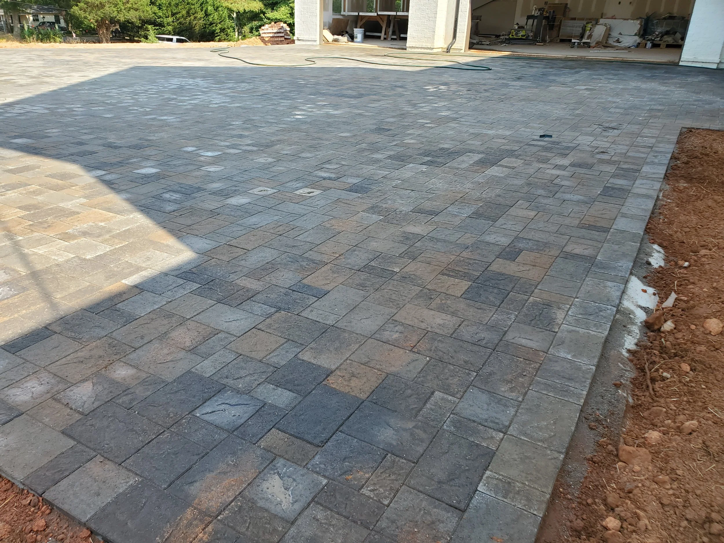 Finished paved driveway extending from garage with construction materials and debris visible inside garage and on a dirt area on the right side.
