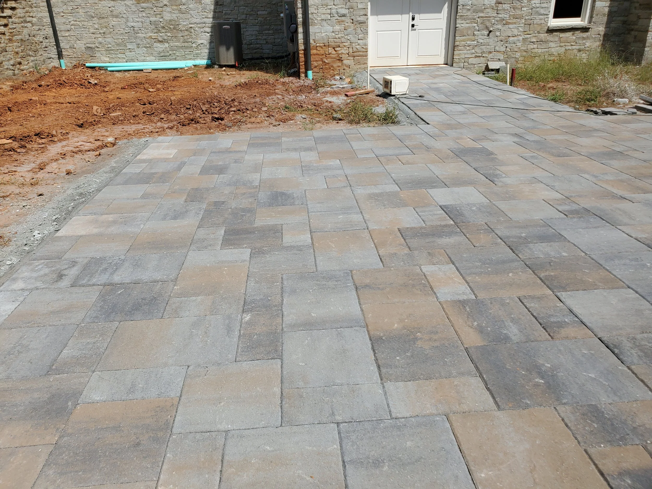 Construction site with paving stones, dirt, and building materials near a stone wall and white door.