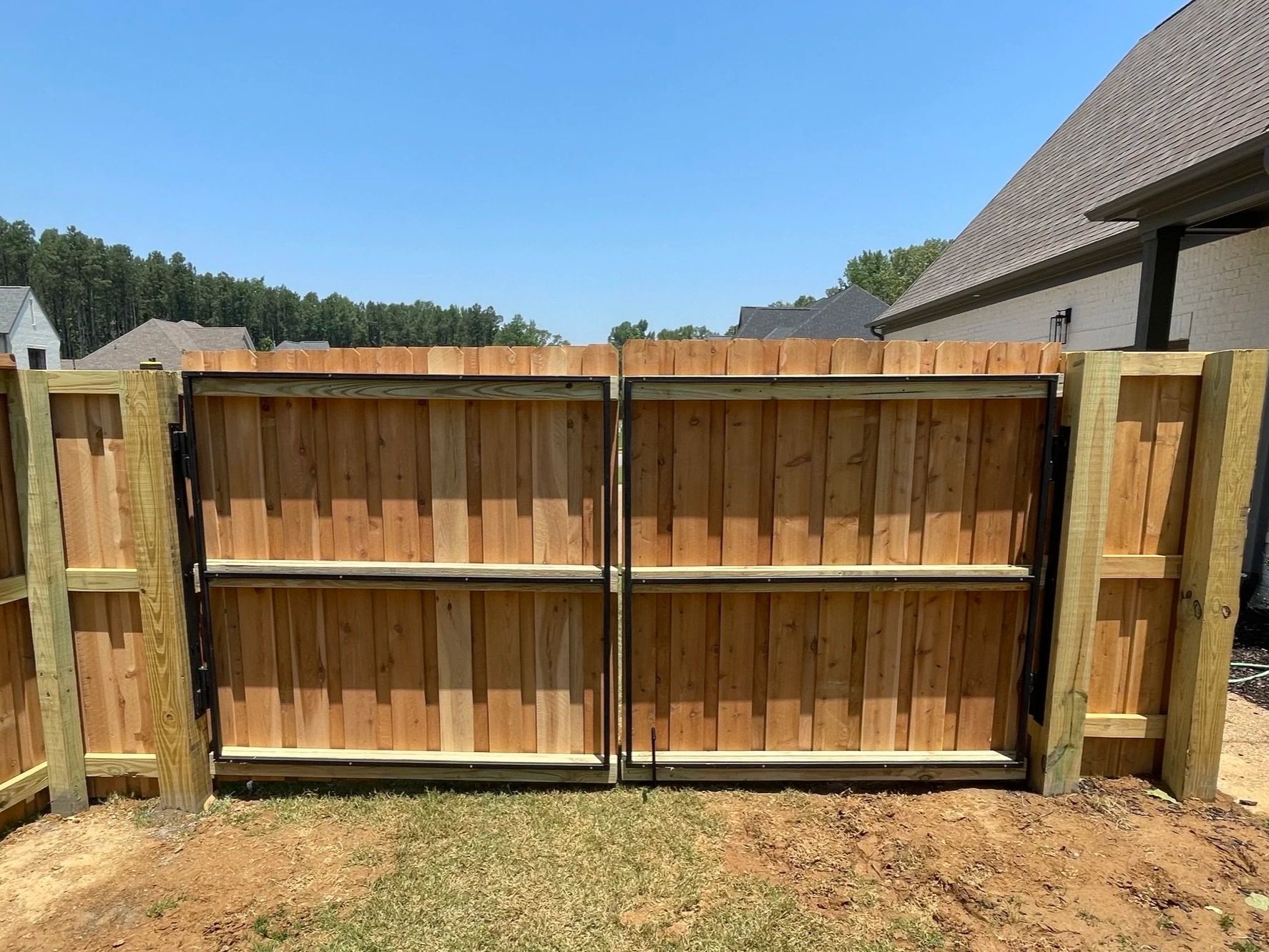 A wooden privacy fence with an open gate under a clear blue sky in a suburban backyard.
