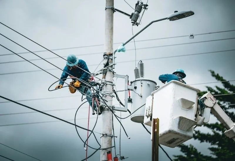 Lineworkers repairing overhead electrical equipment on a utility pole in poor weather conditions
