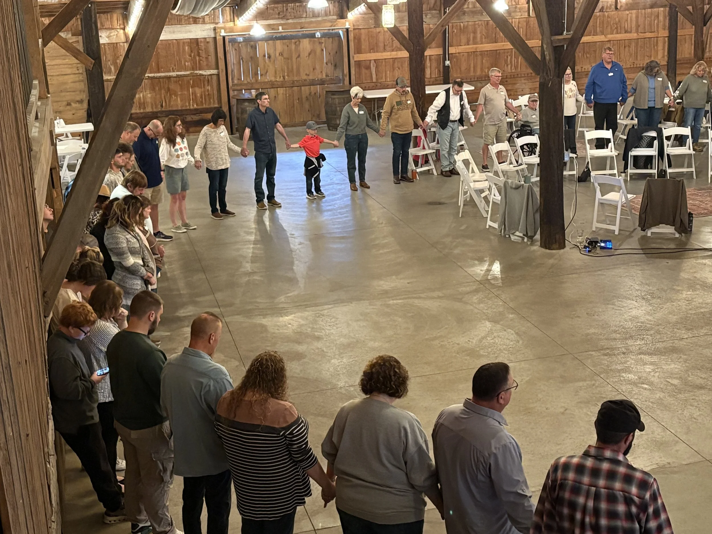 A group of people in a barn, holding hands and praying in a circle.