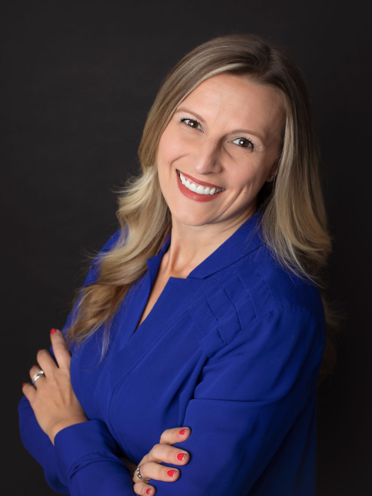 A woman with long blonde hair smiling, wearing a royal blue blouse, against a black background.