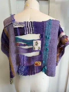 A colorful, patchwork-style knitted or woven garment displayed on a mannequin, featuring various textures and colors like purple, teal, and white.