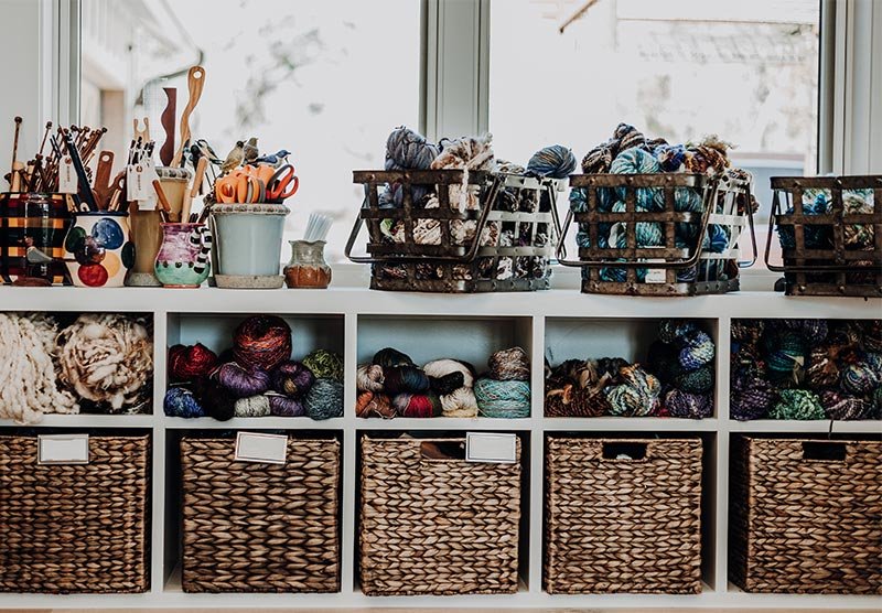 Shelves filled with yarn balls, baskets, and craft supplies in a cozy knitting or craft room.