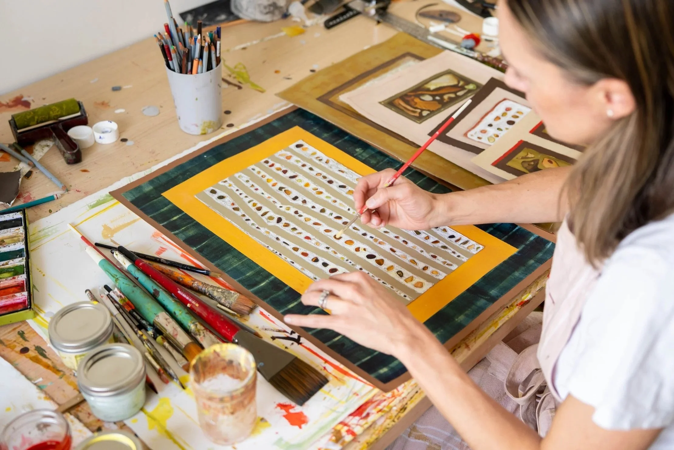An artist working on a canvas with paint and brushes in a studio surrounded by art supplies.