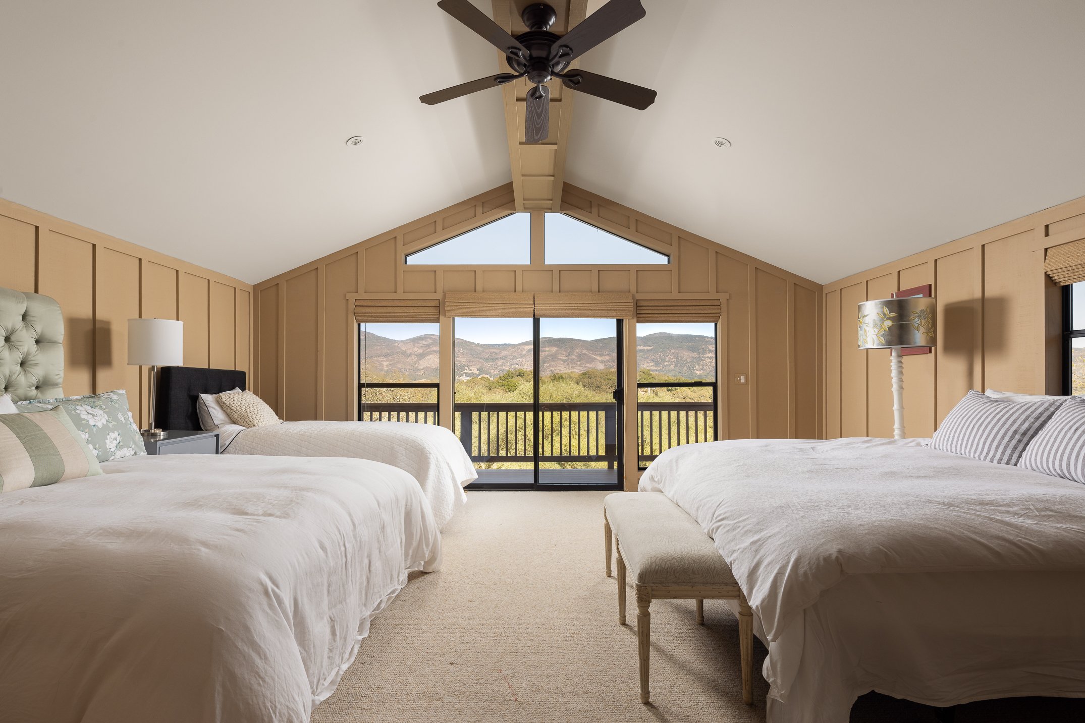 A spacious bedroom with two beds, large windows with blinds, a ceiling fan, and a scenic mountain view outside.