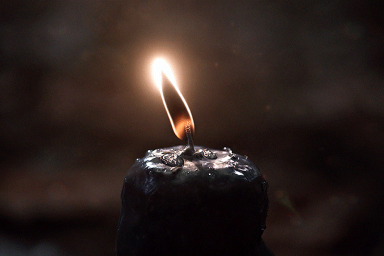 A black candle with a flickering flame on top.