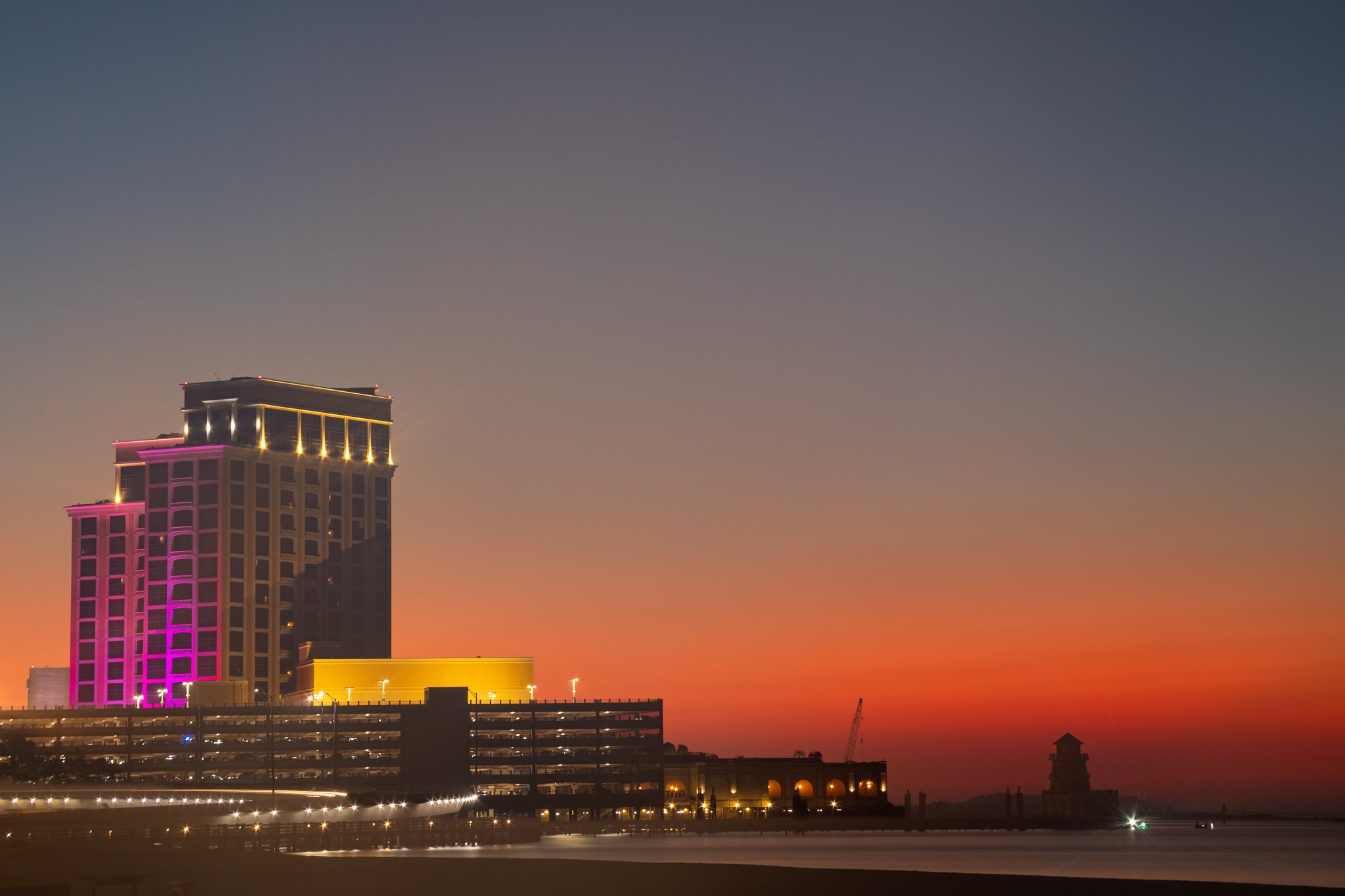 The illuminated Beau Rivage casino rises against a vibrant orange and purple sunrise over Biloxi, Mississippi, as the first light of morning spreads across the Mississippi Gulf Coast.
