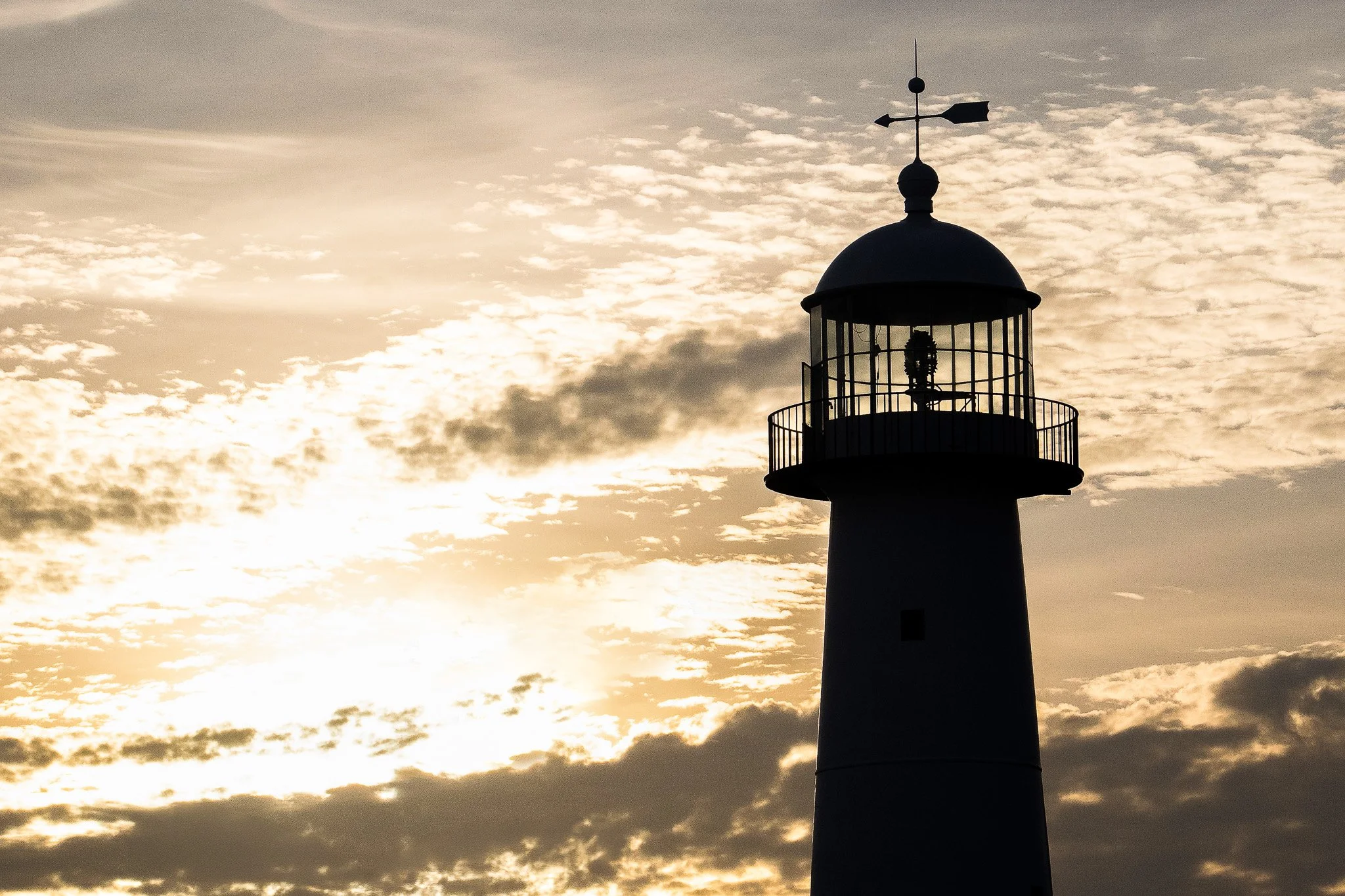 Biloxi Lighthouse silhouetted against a dramatic golden sunset sky.