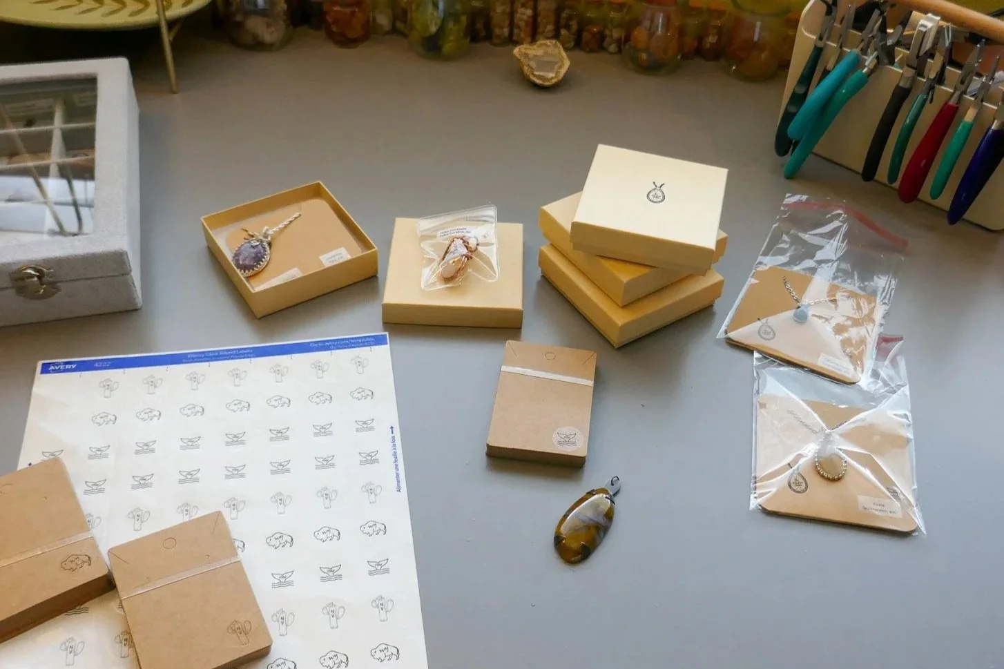 Jewelry items, including necklaces and rings, displayed on a table with packaging and labels, along with pens and a small box.