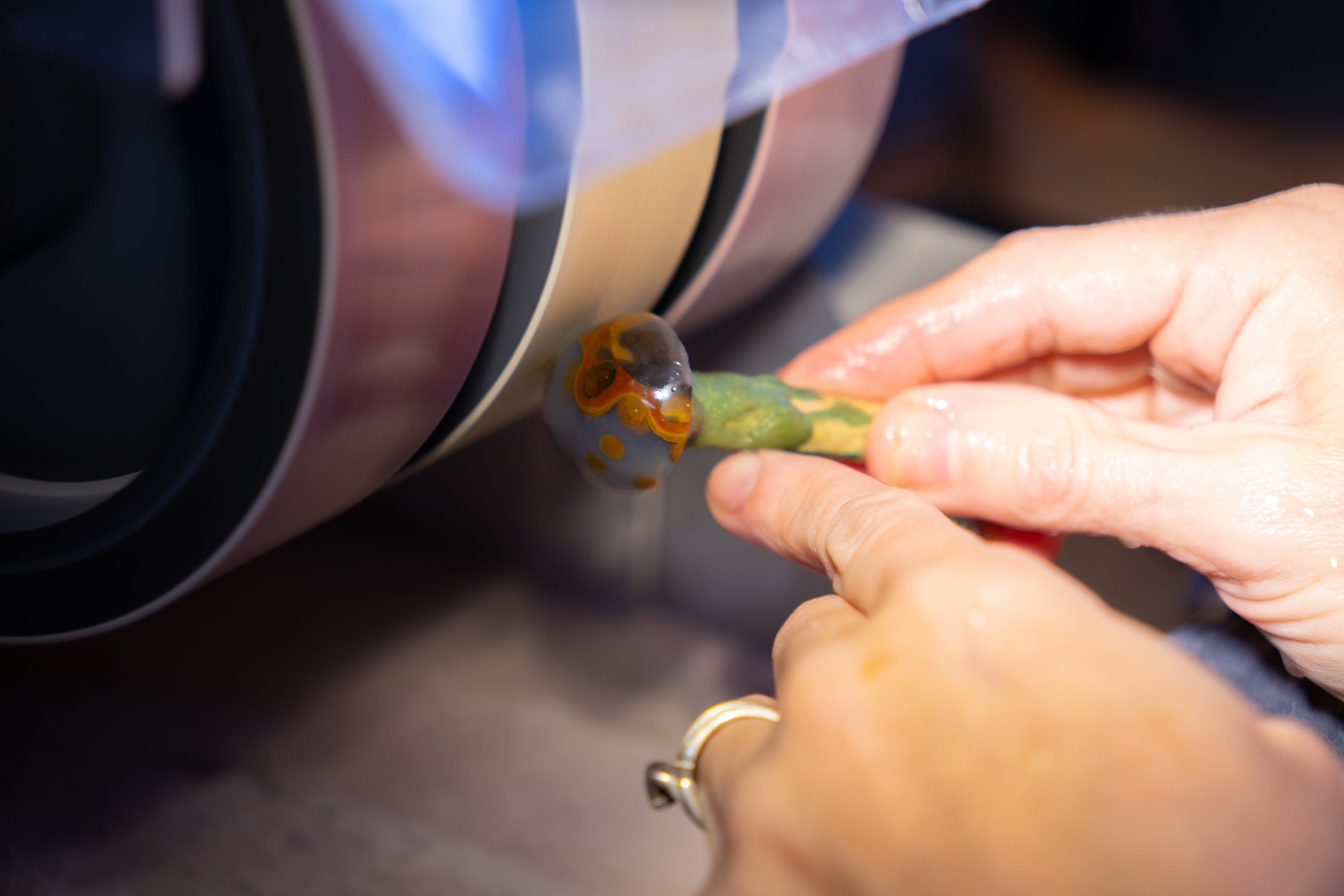 Close-up of a person's hand holding a small object or tool near a shiny, metallic surface, with the background blurred.