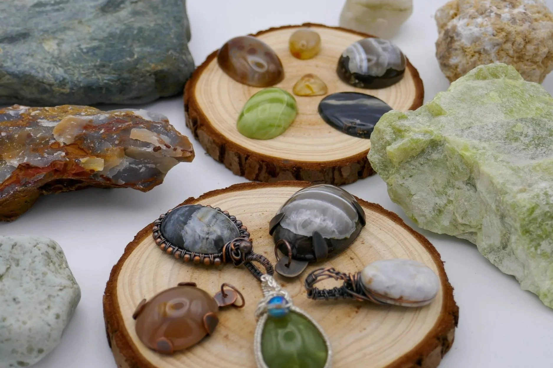 Close-up view of various polished stones and rocks displayed on wooden slices, with some jewelry pieces like pendants and bracelets among them.
