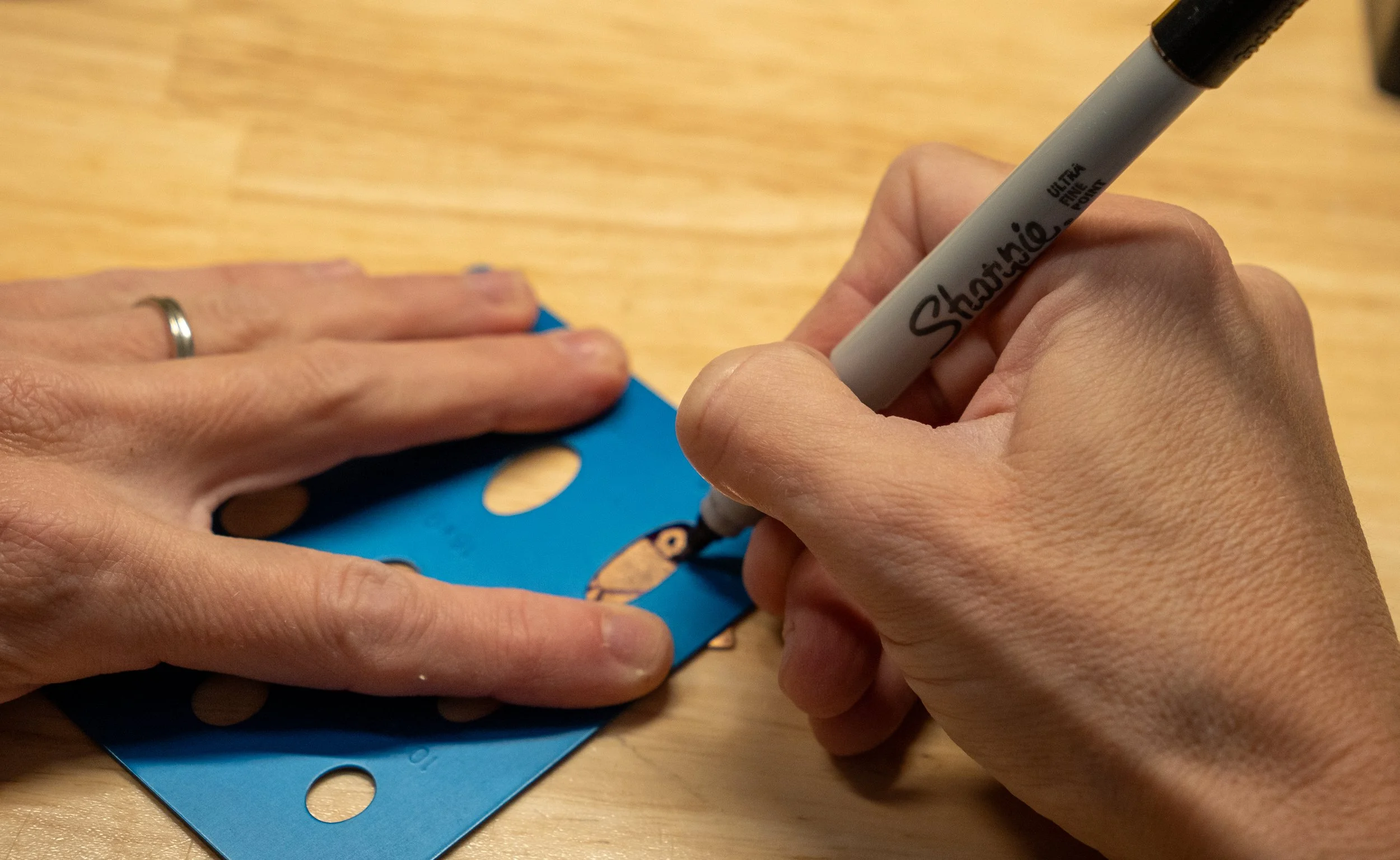 Close-up of hands signing a blue card with a black Sharpie marker, on a wooden surface.