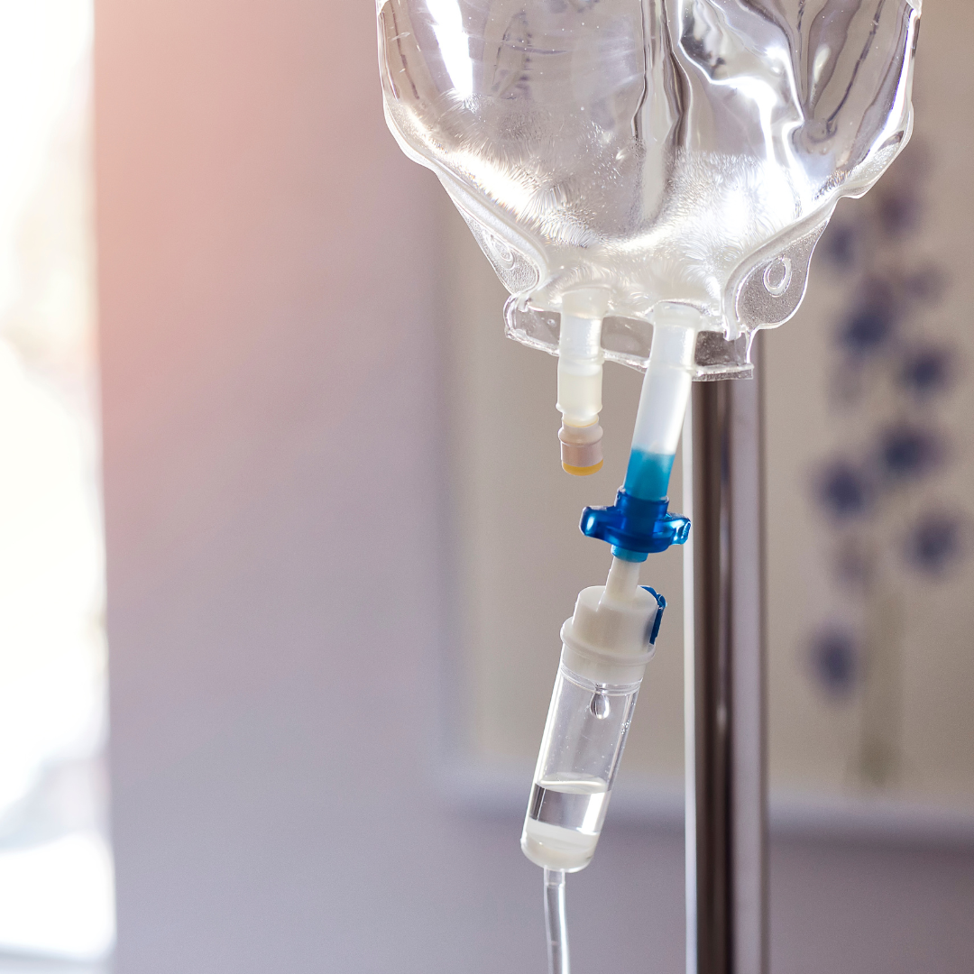 A close-up of an IV drip and tubing with a fluid bag hanging on a metal stand in a medical setting.