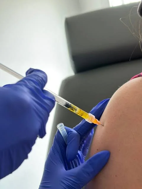 A person receiving a flu shot or vaccination in their upper arm from a healthcare professional wearing blue gloves.