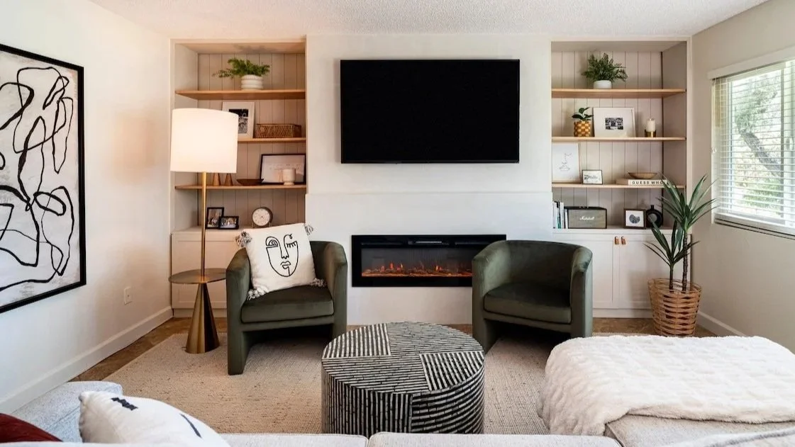 Palm Springs Living room with two green armchairs, a fireplace, a flat-screen TV, built-in bookshelves, a potted plant, and window with blinds.