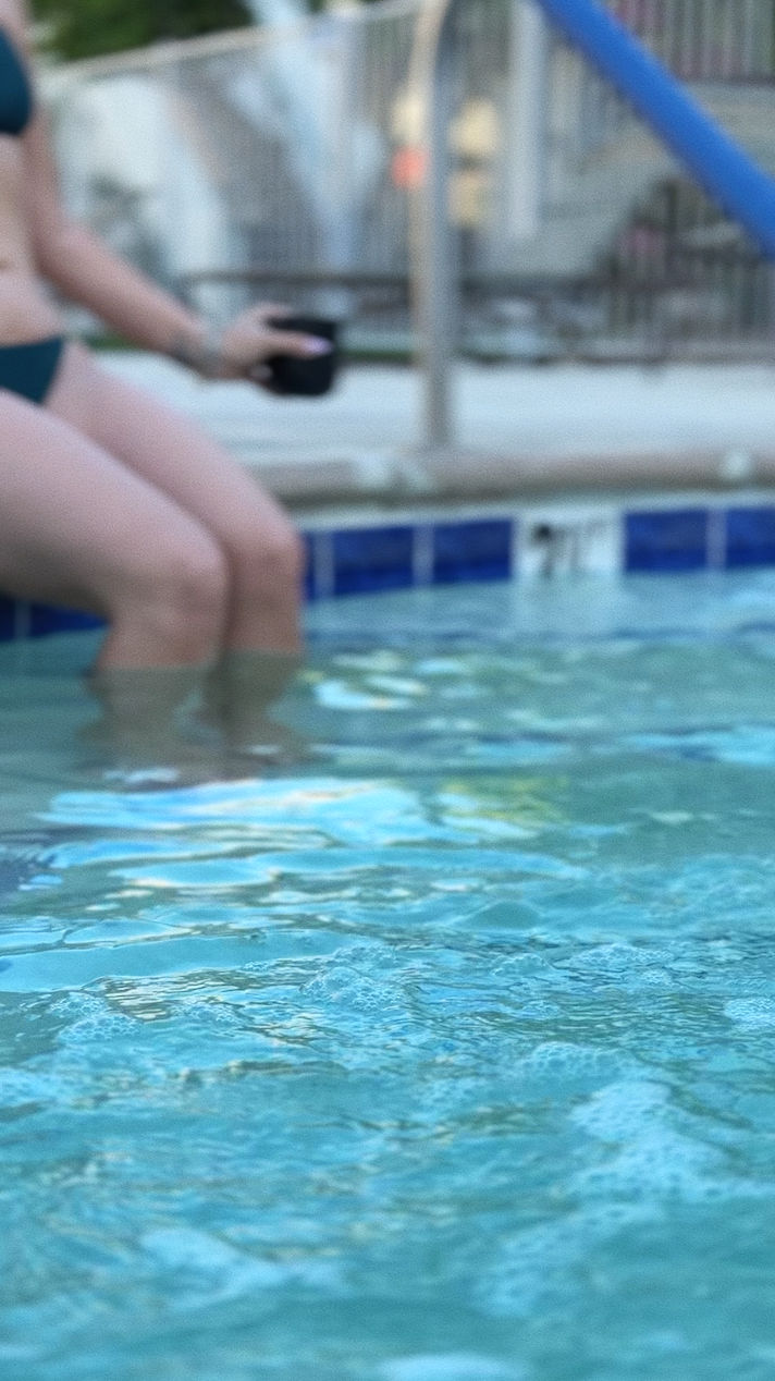 Person sitting at the edge of a swimming pool holding a black cup.