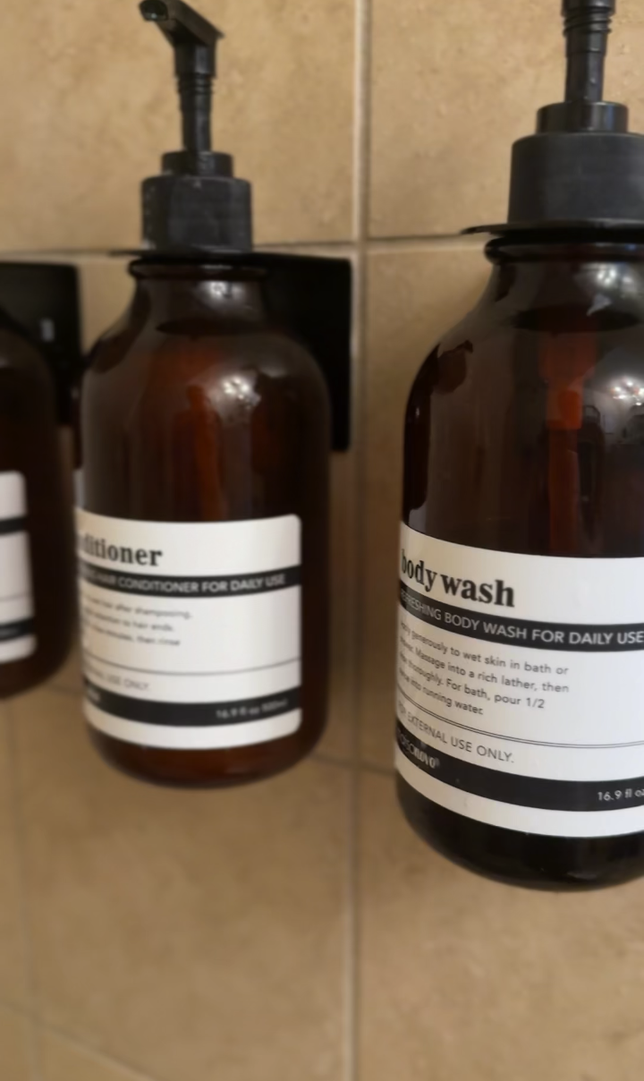 Two brown bottles mounted on a tiled wall, a body wash on the right and a conditioner on the left, with black pump dispensers in Palm Springs vacation rental