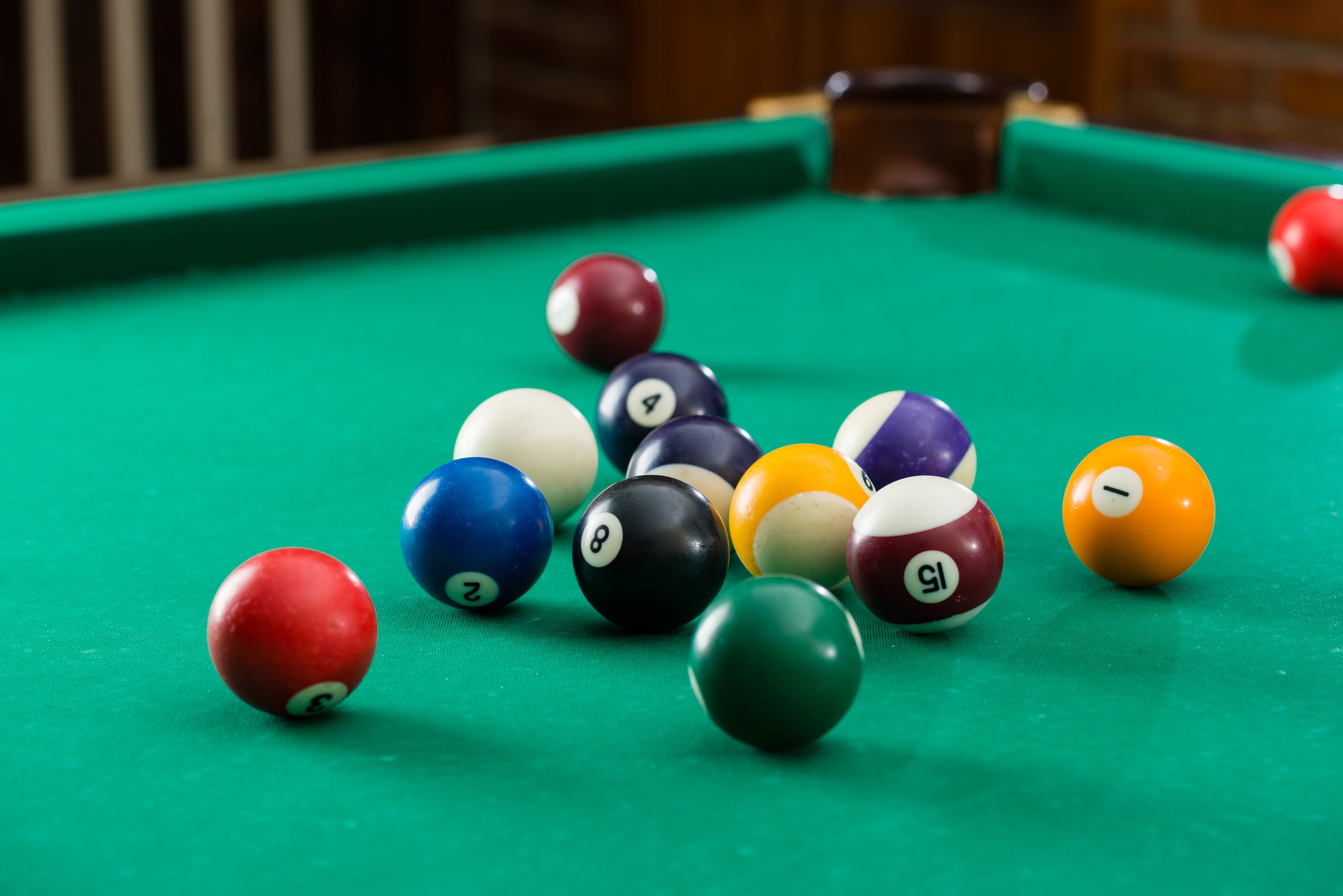 A billiards table with a set of pool balls arranged on the green felt, some balls near the foreground and others near the pockets at the back.