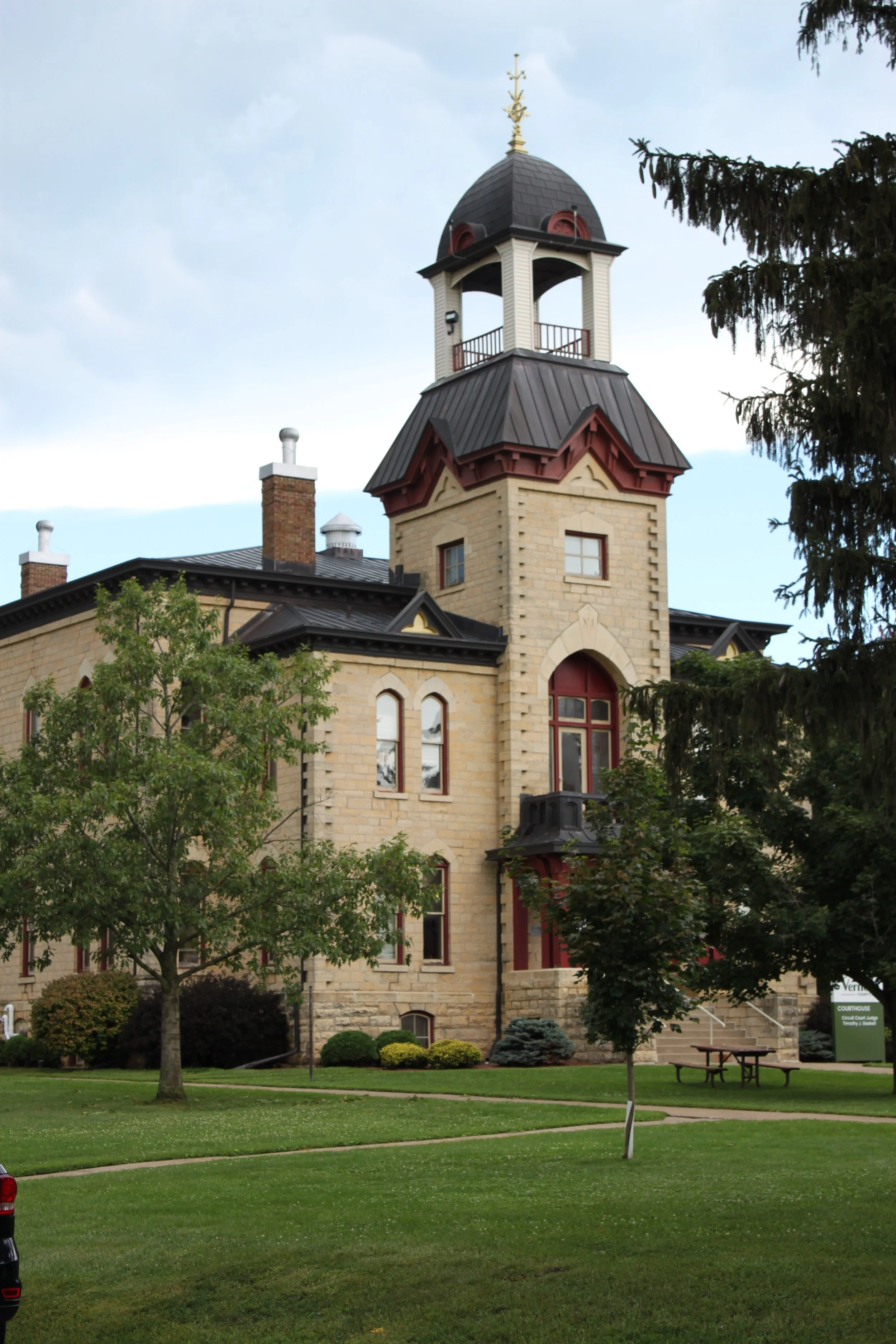 The Vernon County Courthouse with a clock tower in a park with trees, green grass, and a picnic table.