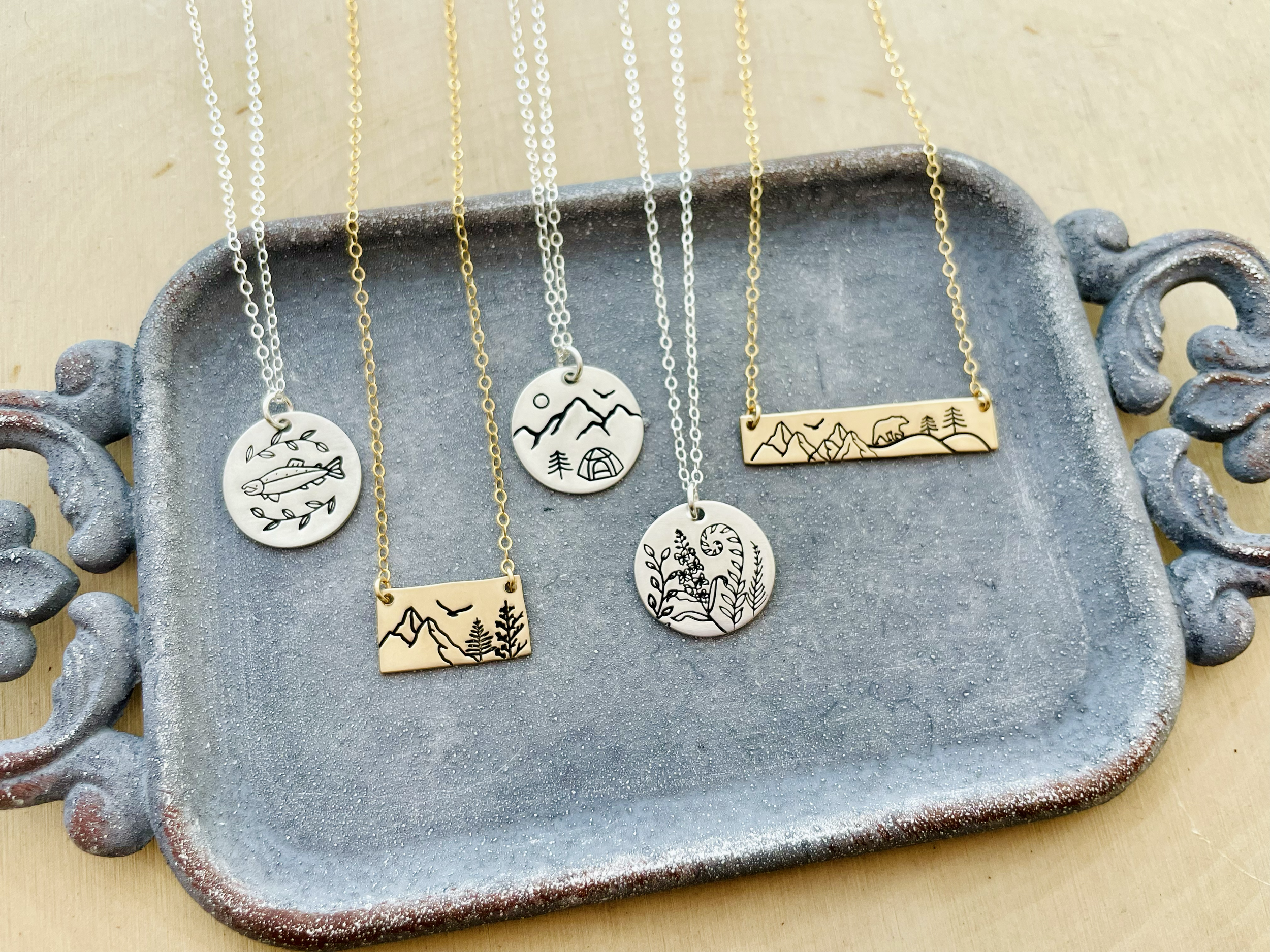 Various necklaces with nature-themed pendants hanging on a rustic, grayish-blue display tray.