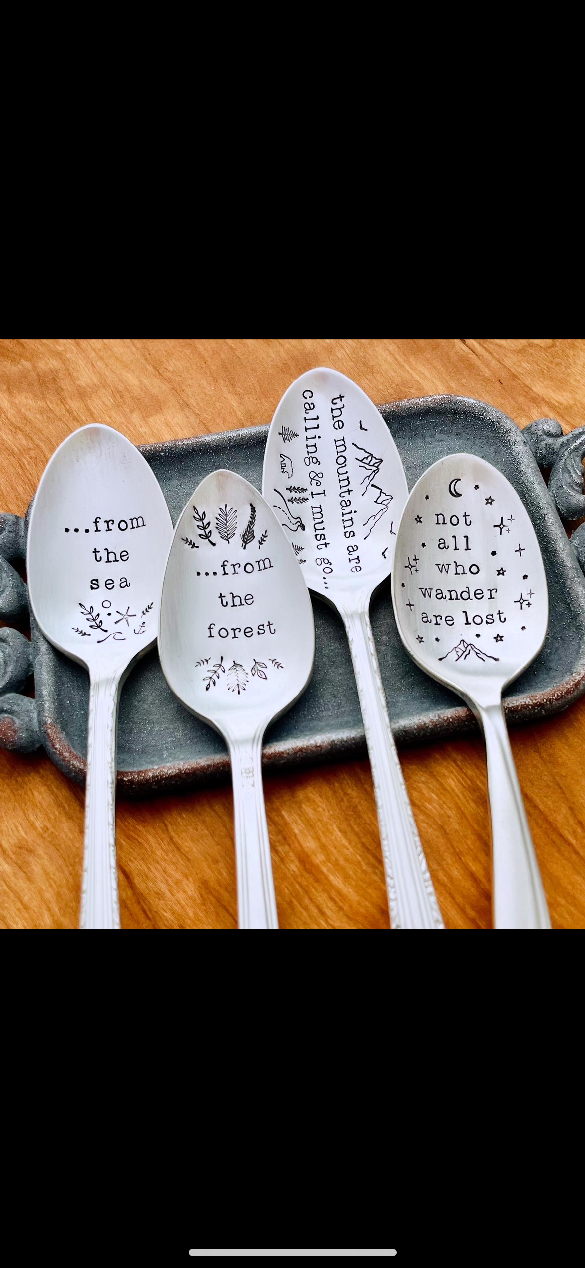 Four white ceramic spoons with black text and illustrations, placed on a rectangular ceramic dish on a wooden surface, with poetic quotes about nature and exploration.