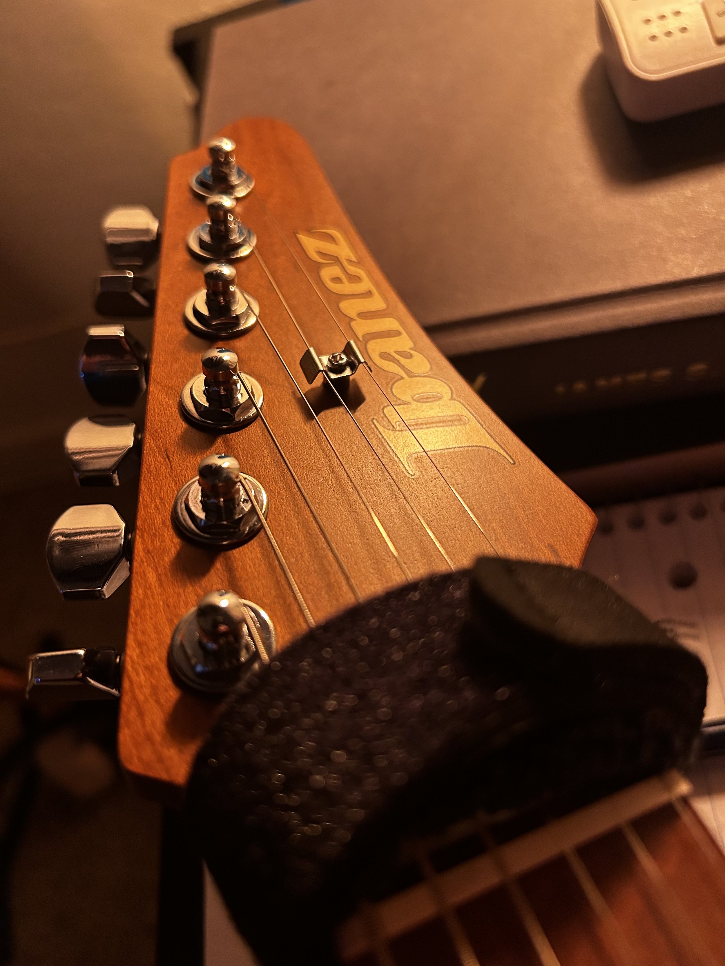 Close-up of the headstock of an orange-colored guitar with tuning pegs and the word "Fender" written on it.