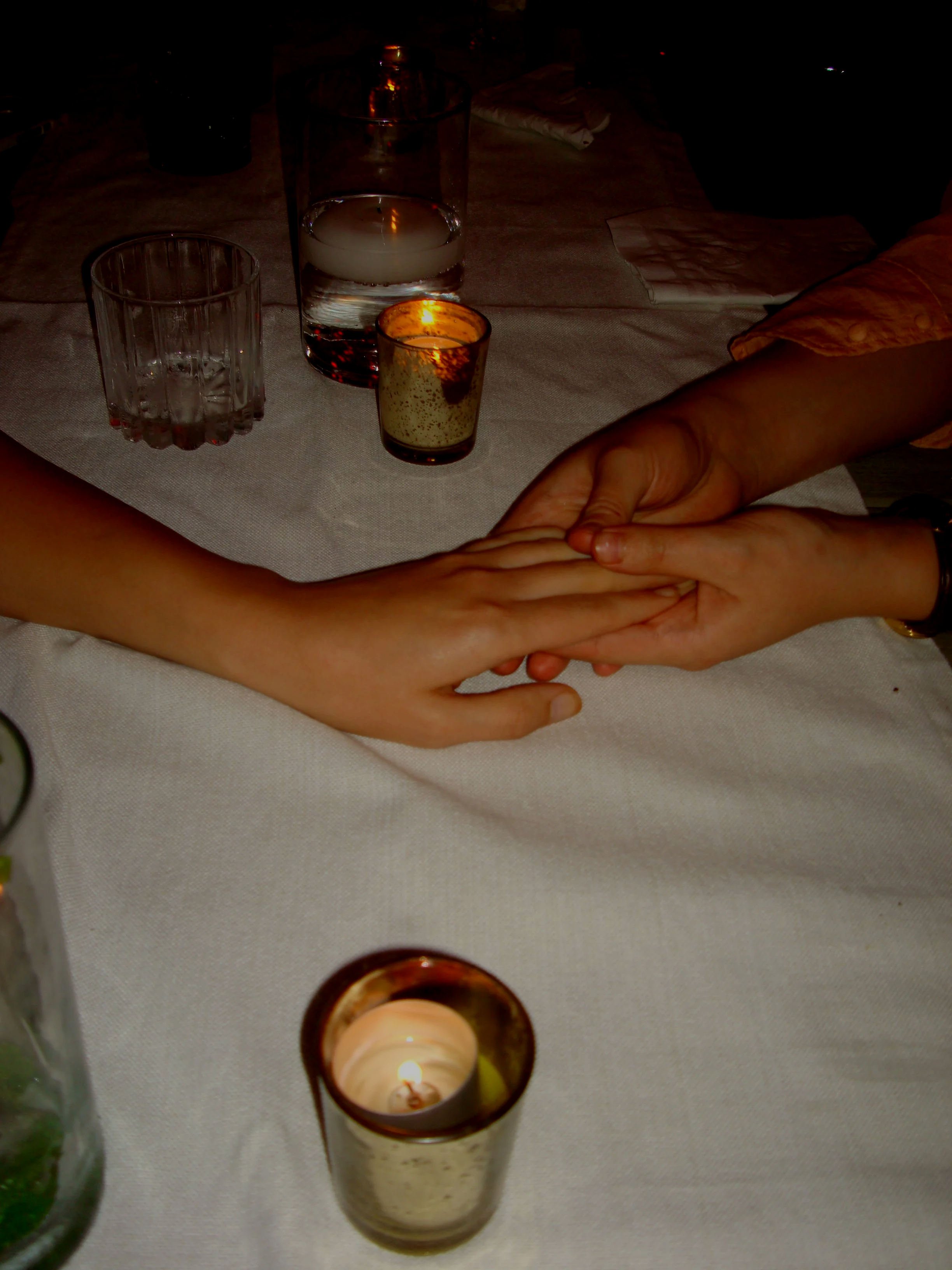 Table decorated with glasses, a candle, a napkin, and two women holding hands.