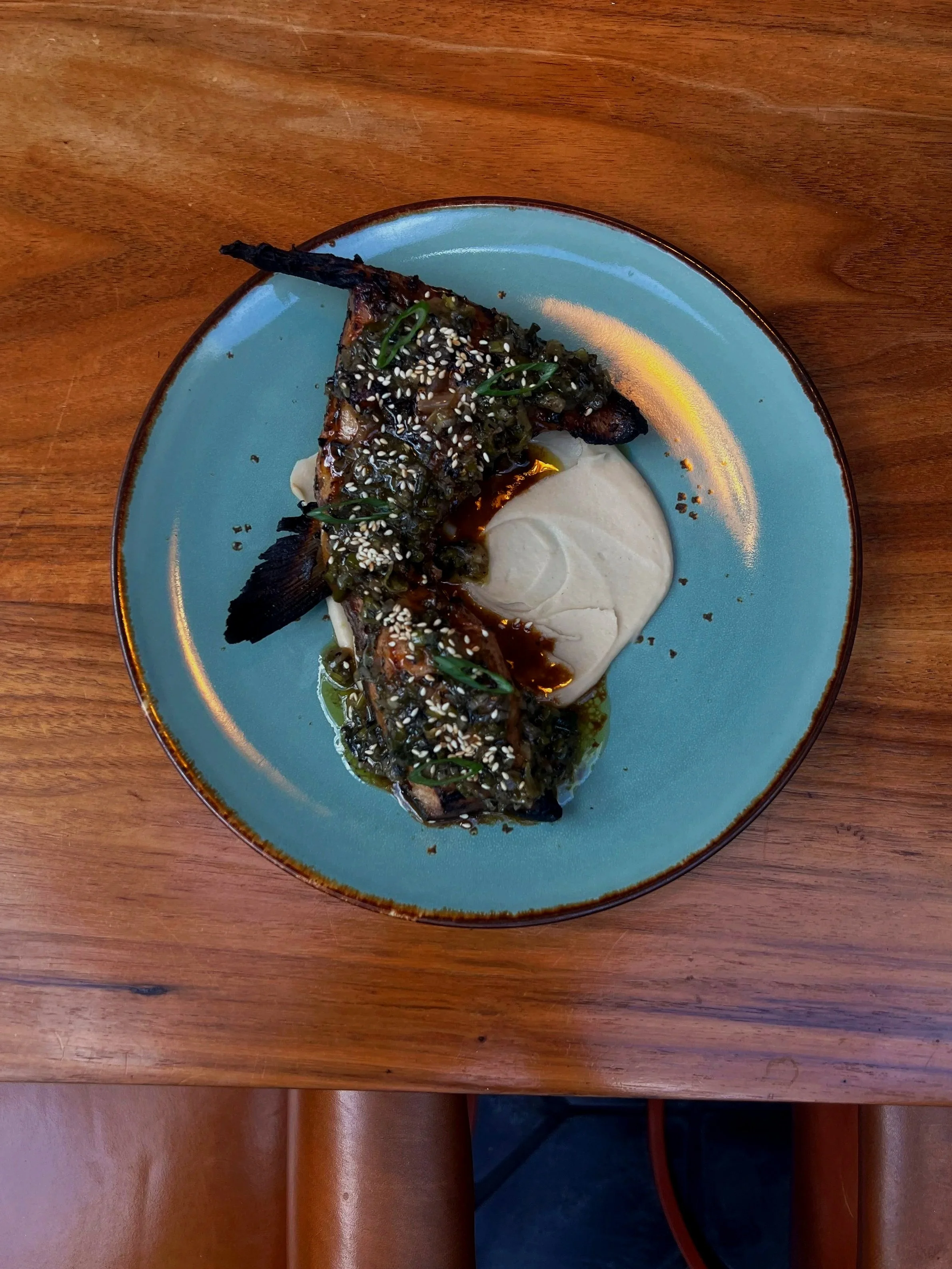Grilled hamachi collar with scallion salsa verde, white bean puree, and sesame seeds on an ornate blue speckled plate.