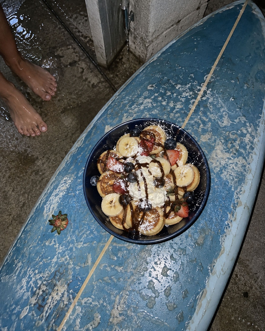 TideHaus mini pancake bowl with fruit, whipped cream and chocolate drizzle displayed on a blue surfboard.
